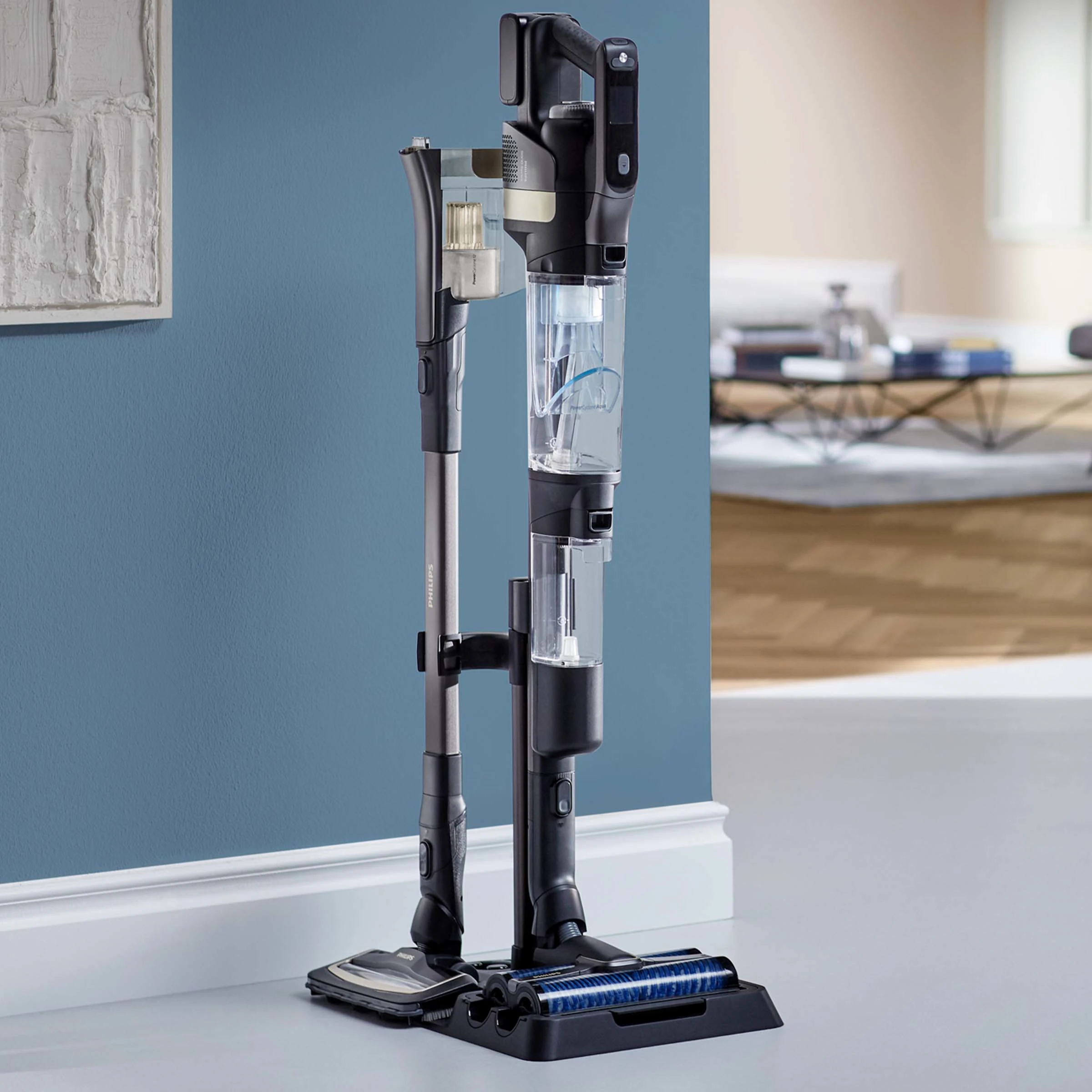 Czarno-szary odkurzacz stoi na podstawie. Odkurzacz ma długi uchwyt i zbiornik na wodę.