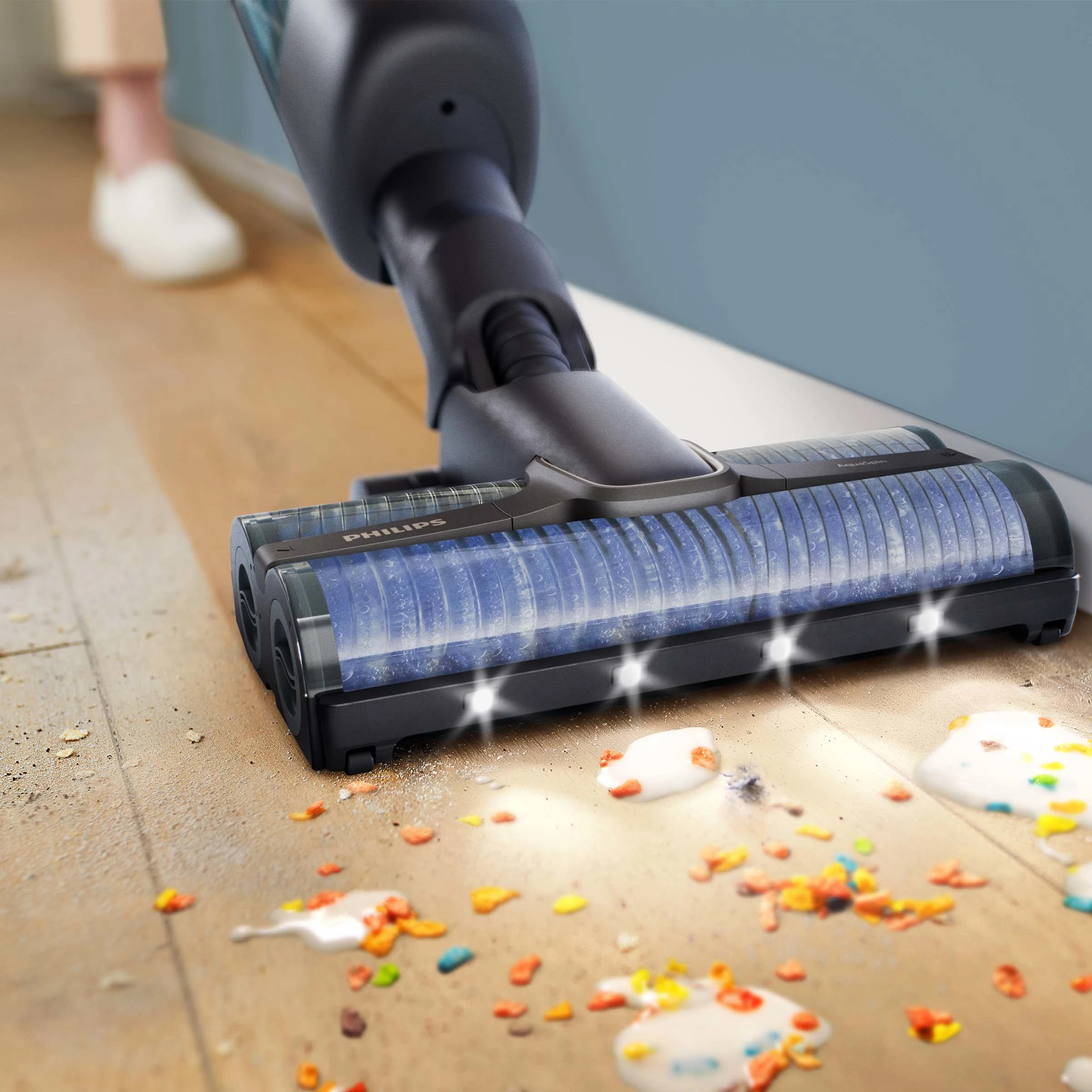 Głowica odkurzacza czyści drewnianą podłogę. Na podłodze są kolorowe plamy.