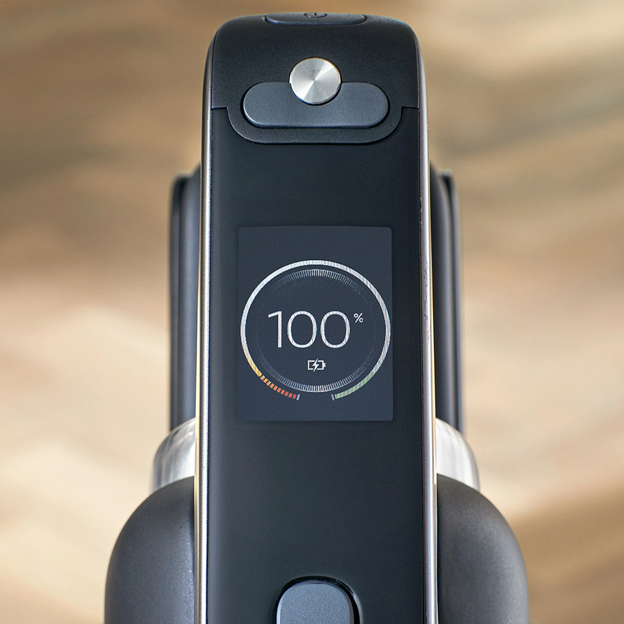 Czarne urządzenie z ekranem wyświetlającym 100% naładowania baterii. Urządzenie ma przycisk i port ładowania.