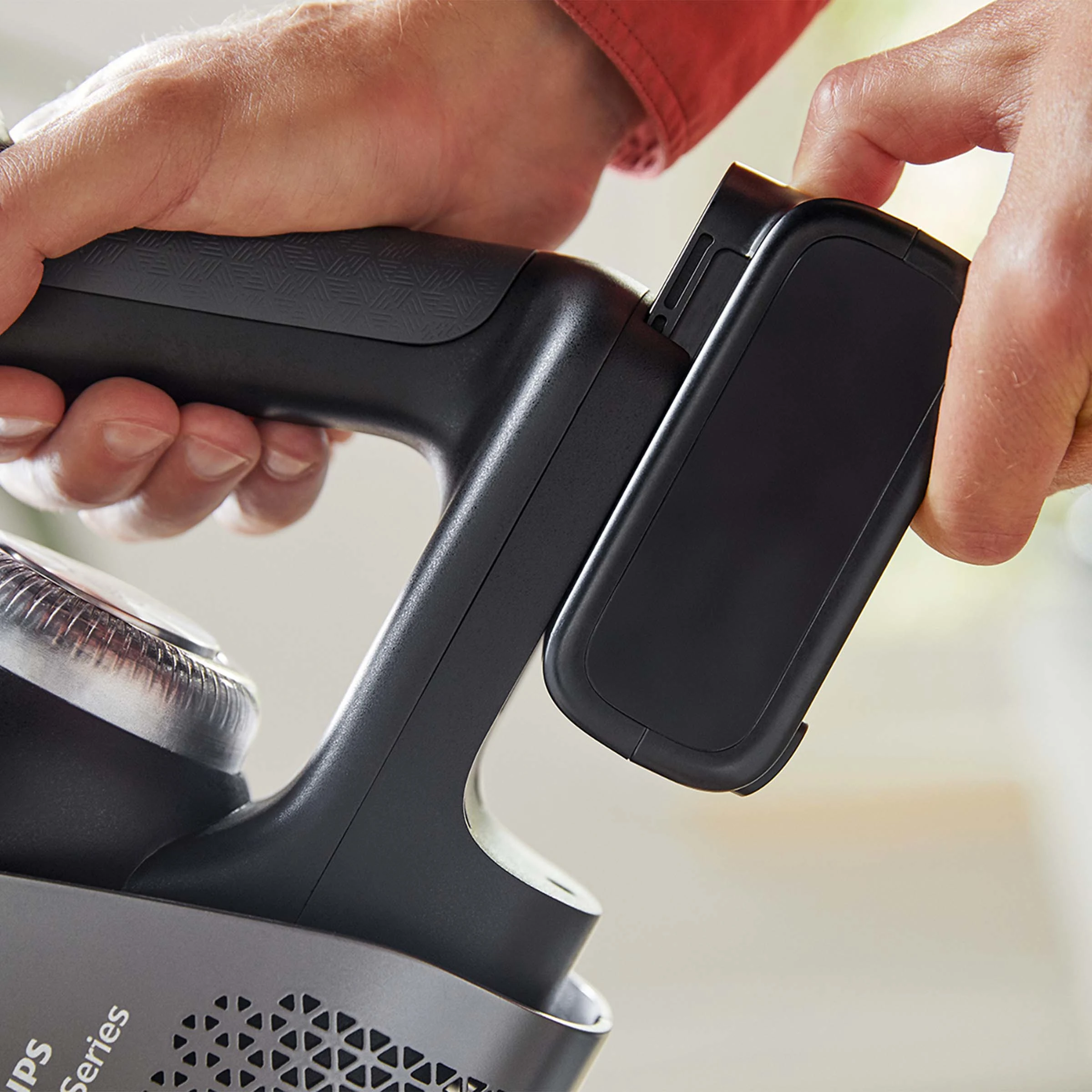 Dłonie trzymające czarny akumulator do odkurzacza, mocujące go do urządzenia.