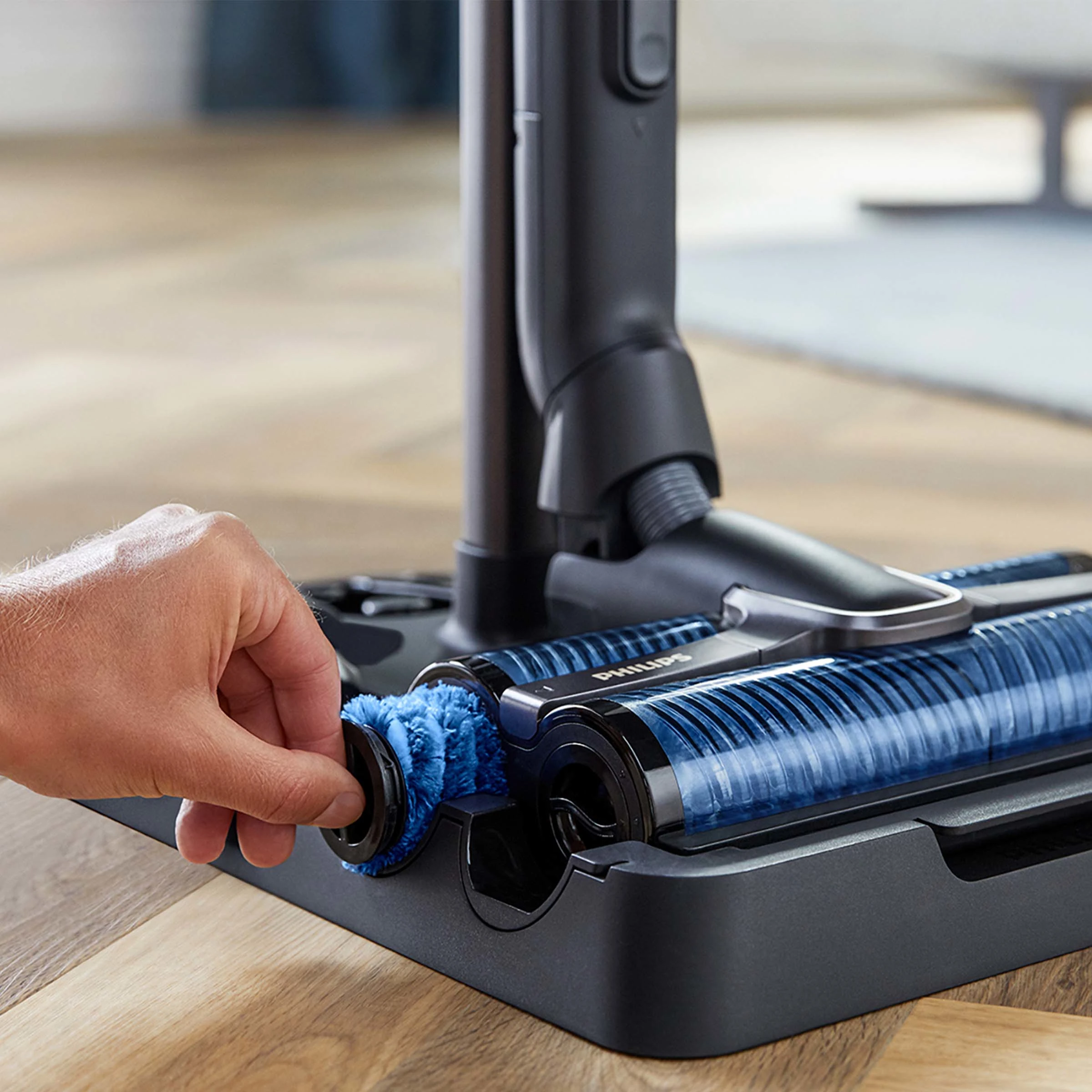 Dłoń wyjmująca szczotkę z czarnej podstawy odkurzacza, ujęcie z bliska.