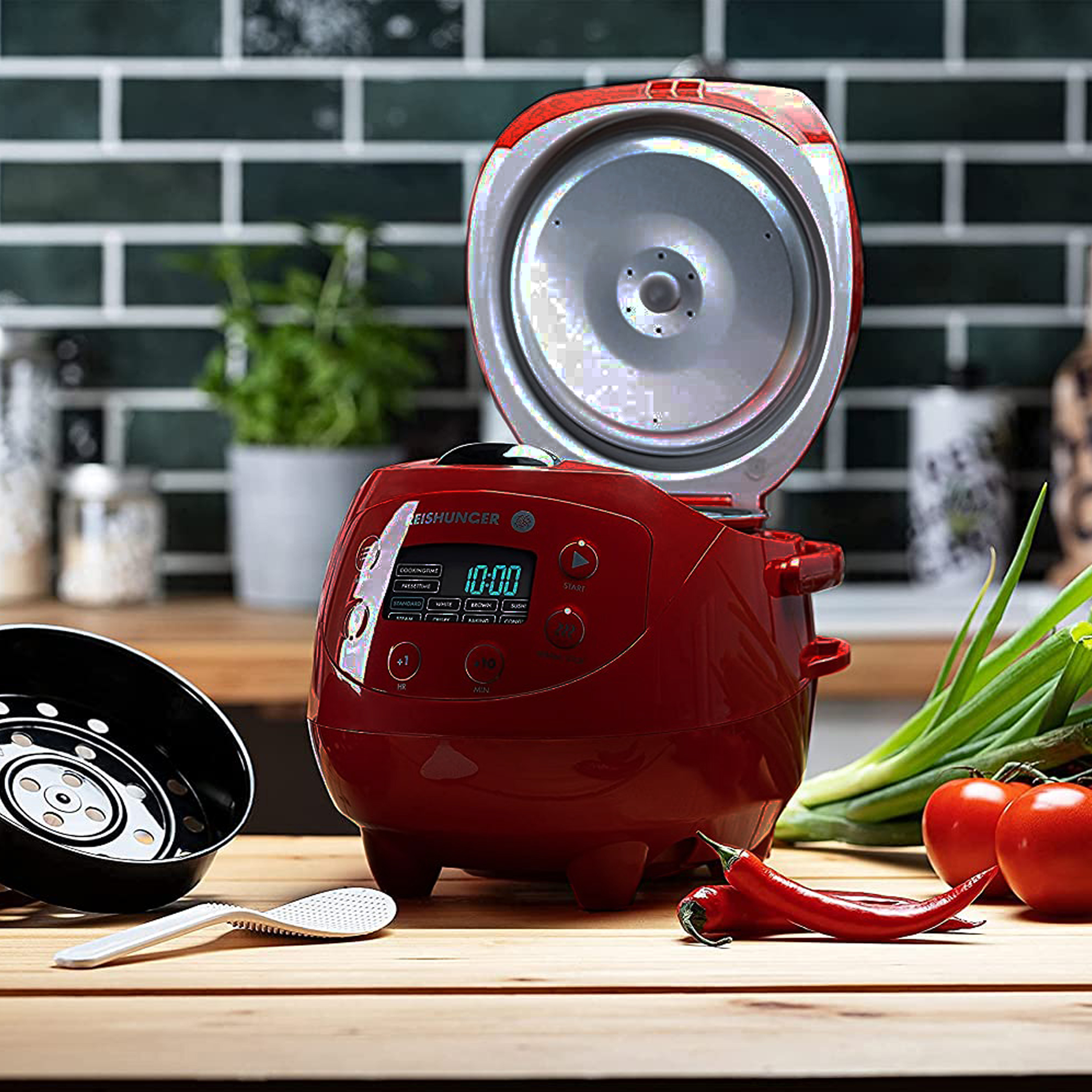 Ein roter Reiskocher mit Digitalanzeige, offenem Deckel und Zutaten wie Tomaten und Chilischoten.