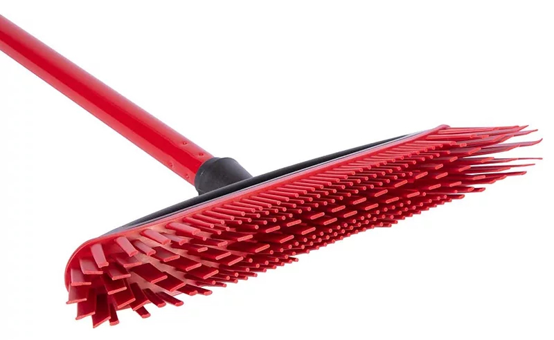 Czerwona miotła z czerwonym włosiem, czarnym uchwytem, na białym tle. Ukośnie do widza.