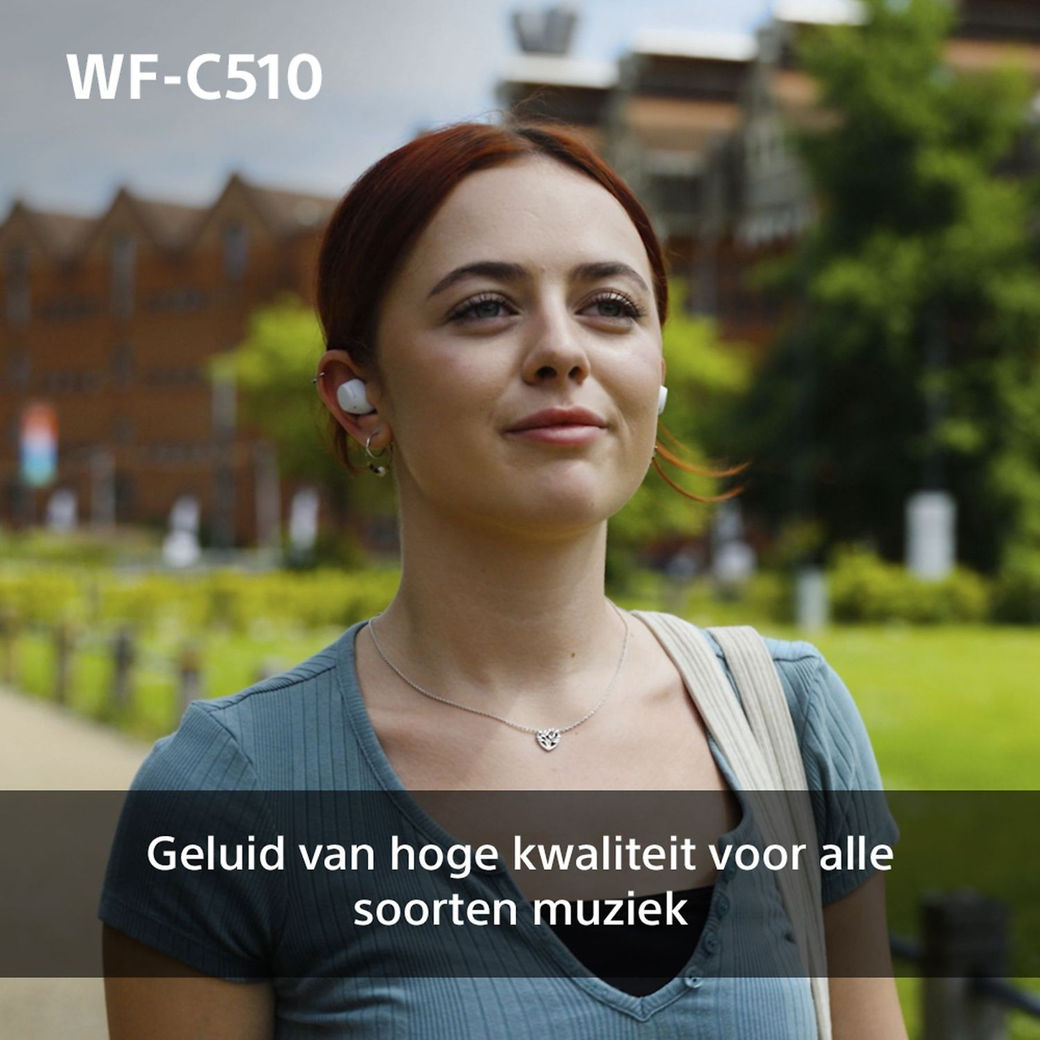 Woman wearing white earbuds, smiling, looking up. Background has greenery and a building.