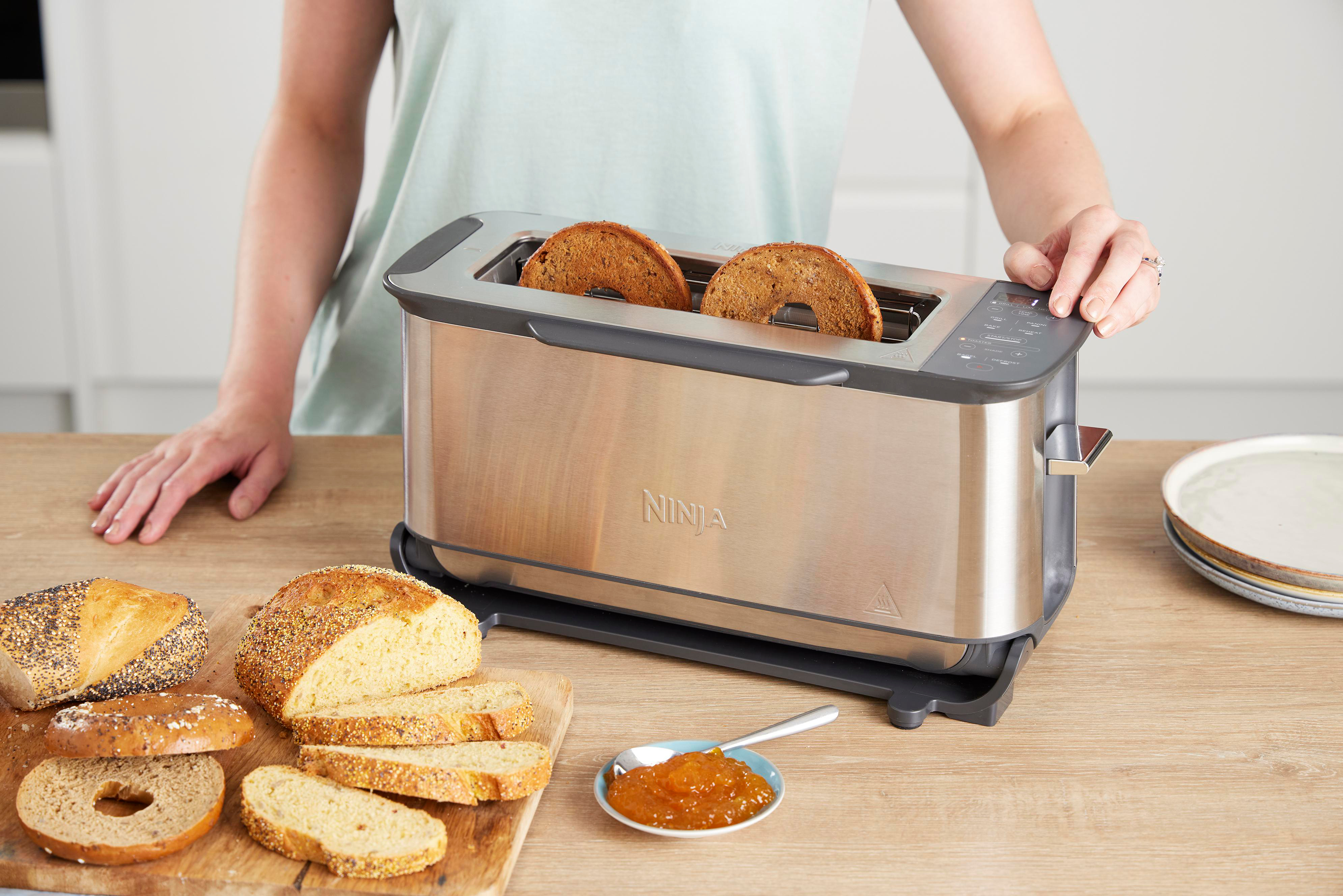 Ein Toaster mit zwei Scheiben Toastbrot. Brotscheiben und ein Glas Marmelade stehen auf dem Tisch.