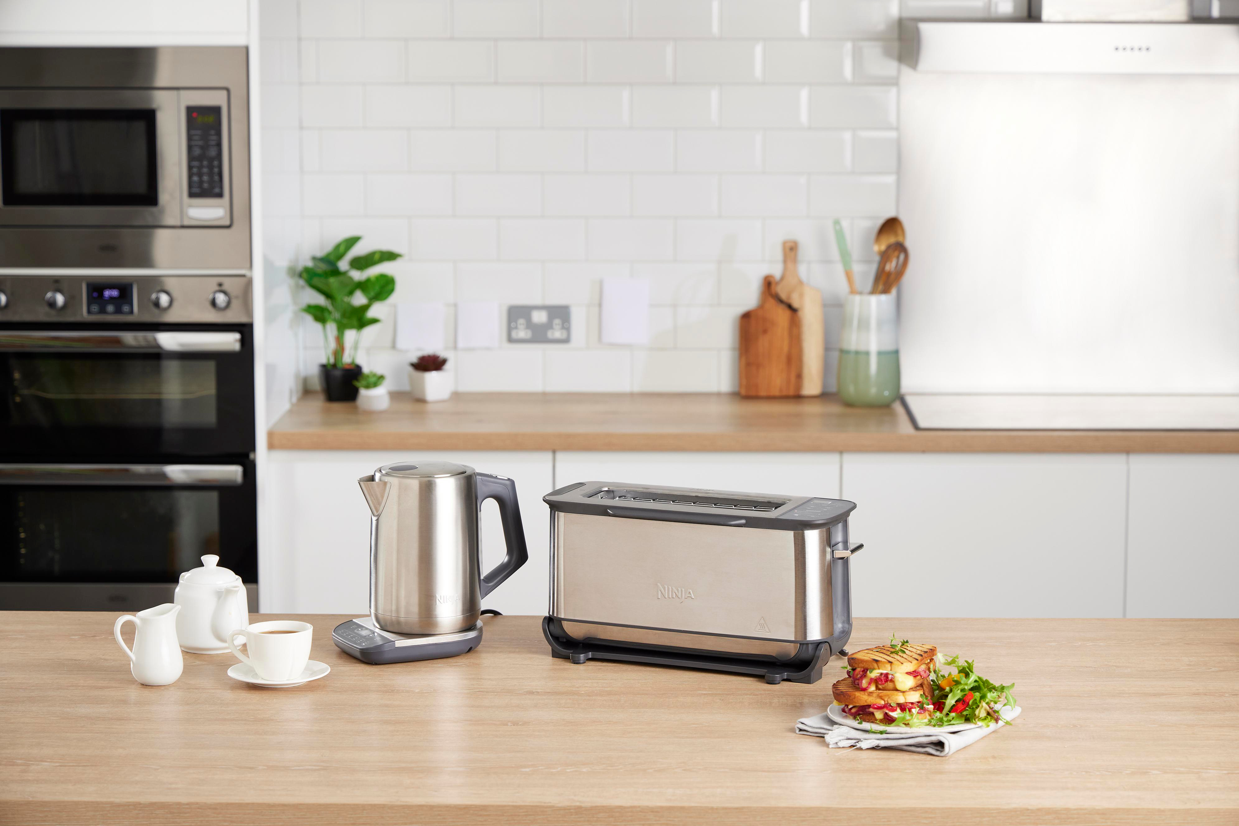 Küchenszene mit Wasserkocher, Toaster und Essen auf dem Tisch. Mikrowelle und Ofen im Hintergrund.