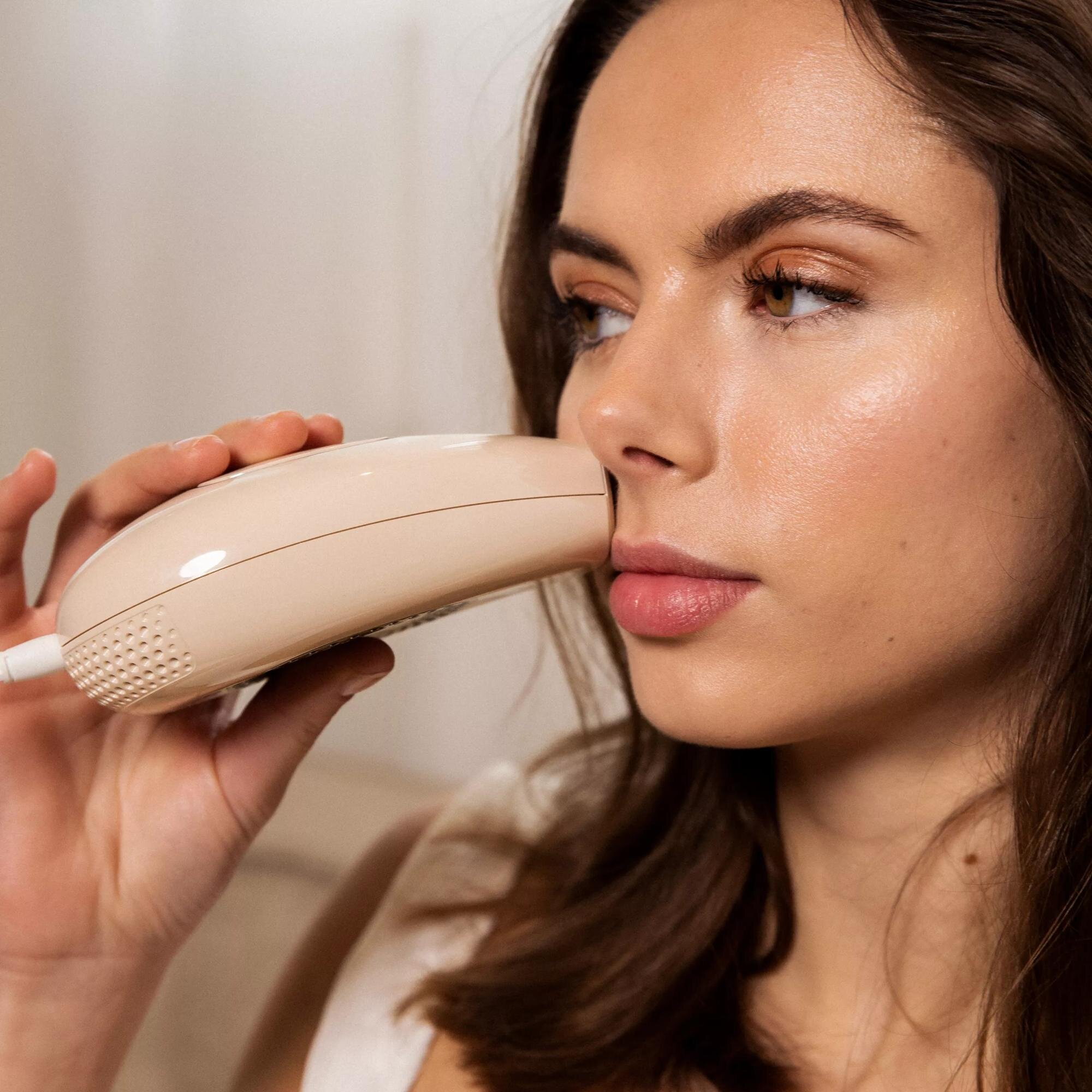Kobieta trzyma beżowe urządzenie przy nosie, prawdopodobnie do zabiegu kosmetycznego.