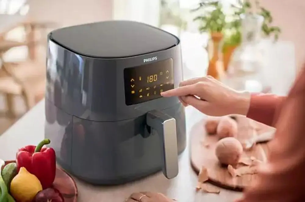 Frytownica beztłuszczowa. Osoba dotyka panelu sterowania. Warzywa i jedzenie na drewnianej desce.