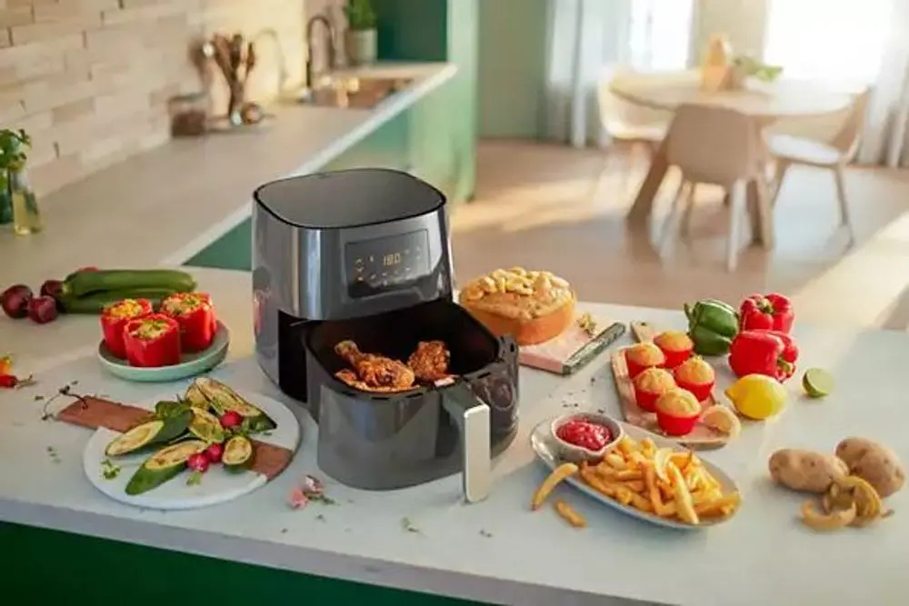Scena kuchenna, frytownica powietrzna z jedzeniem, warzywami i nakrytym stołem.