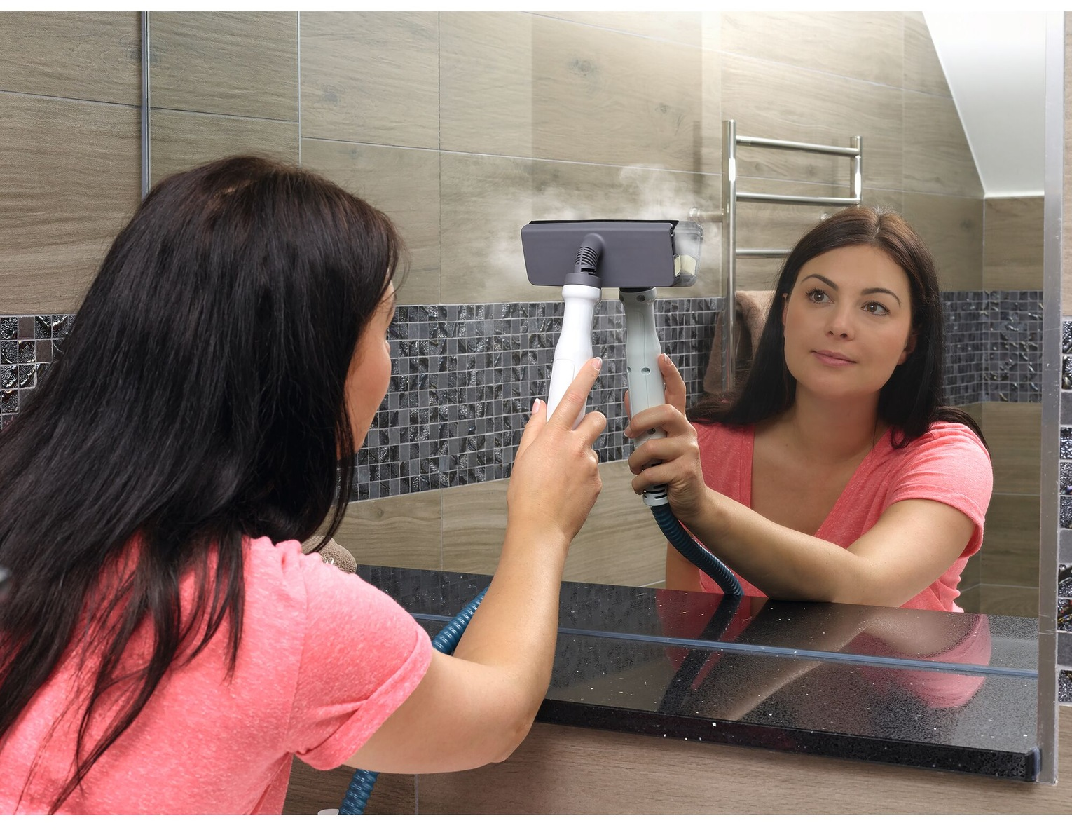 Une femme nettoie un miroir avec un nettoyeur vapeur, reflétant son visage.