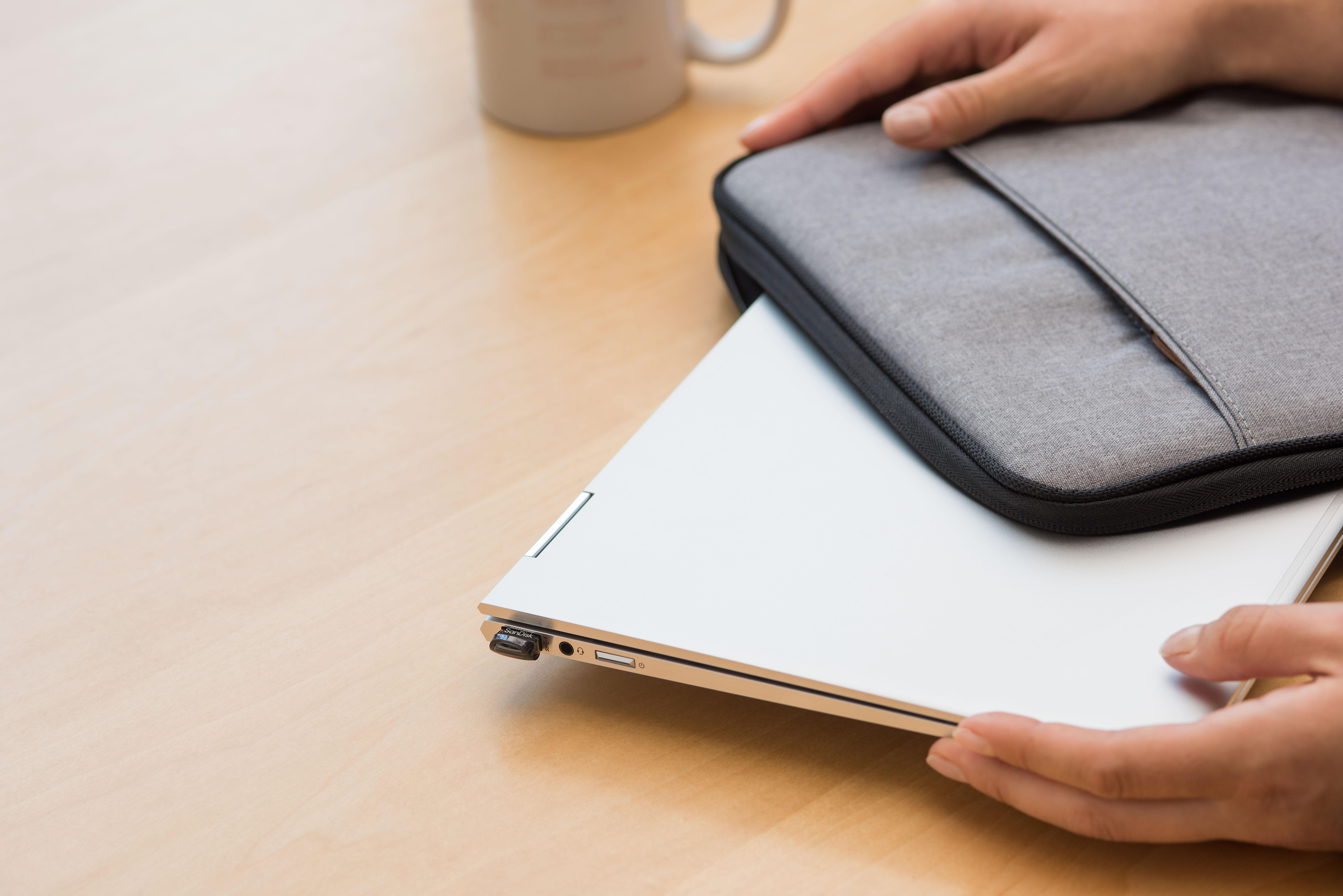 Hände halten einen silbernen Laptop in einem grauen Etui, im Hintergrund eine Tasse.