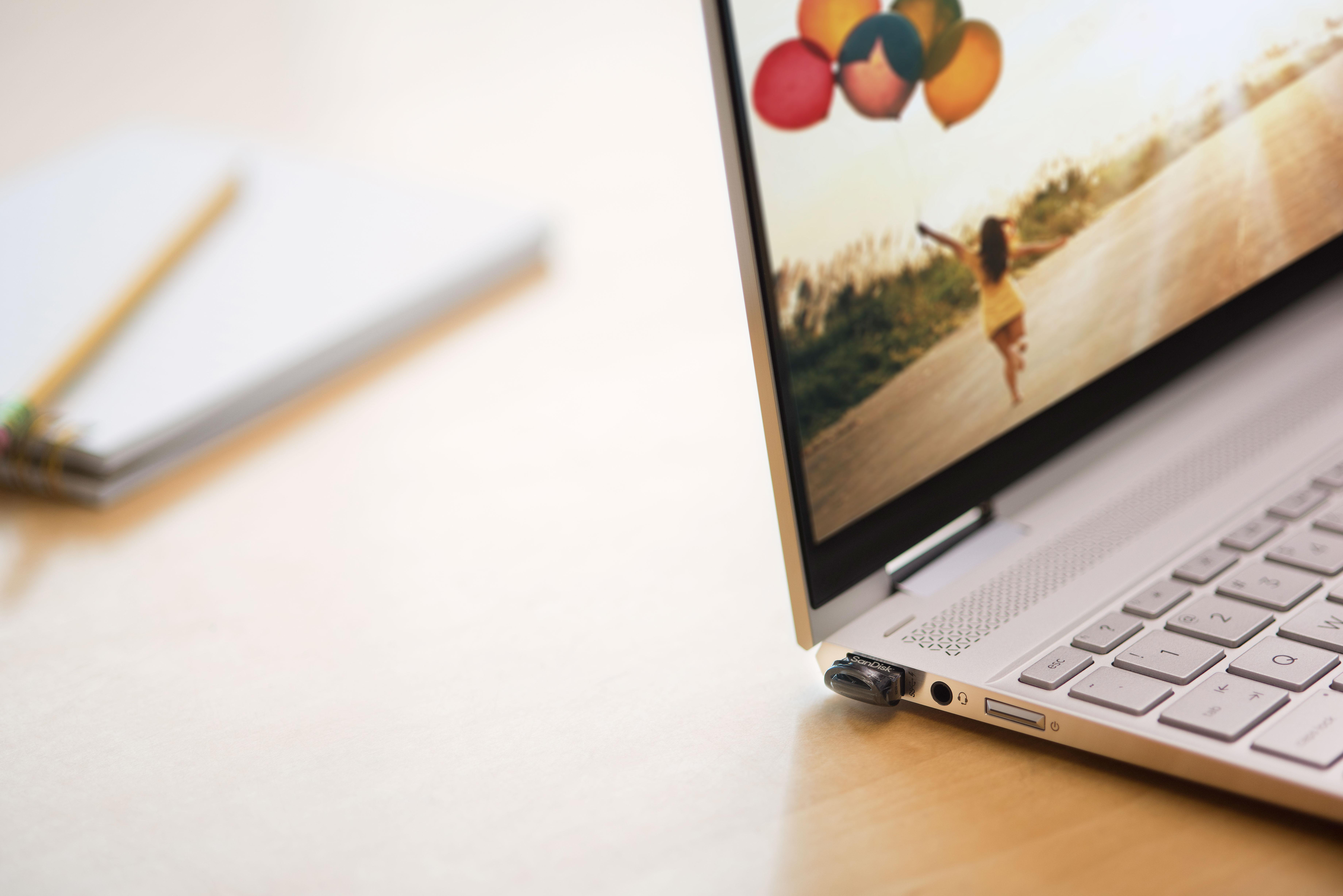 Laptop geöffnet, zeigt Foto einer Frau mit Ballons, neben Notizblock und Bleistift.