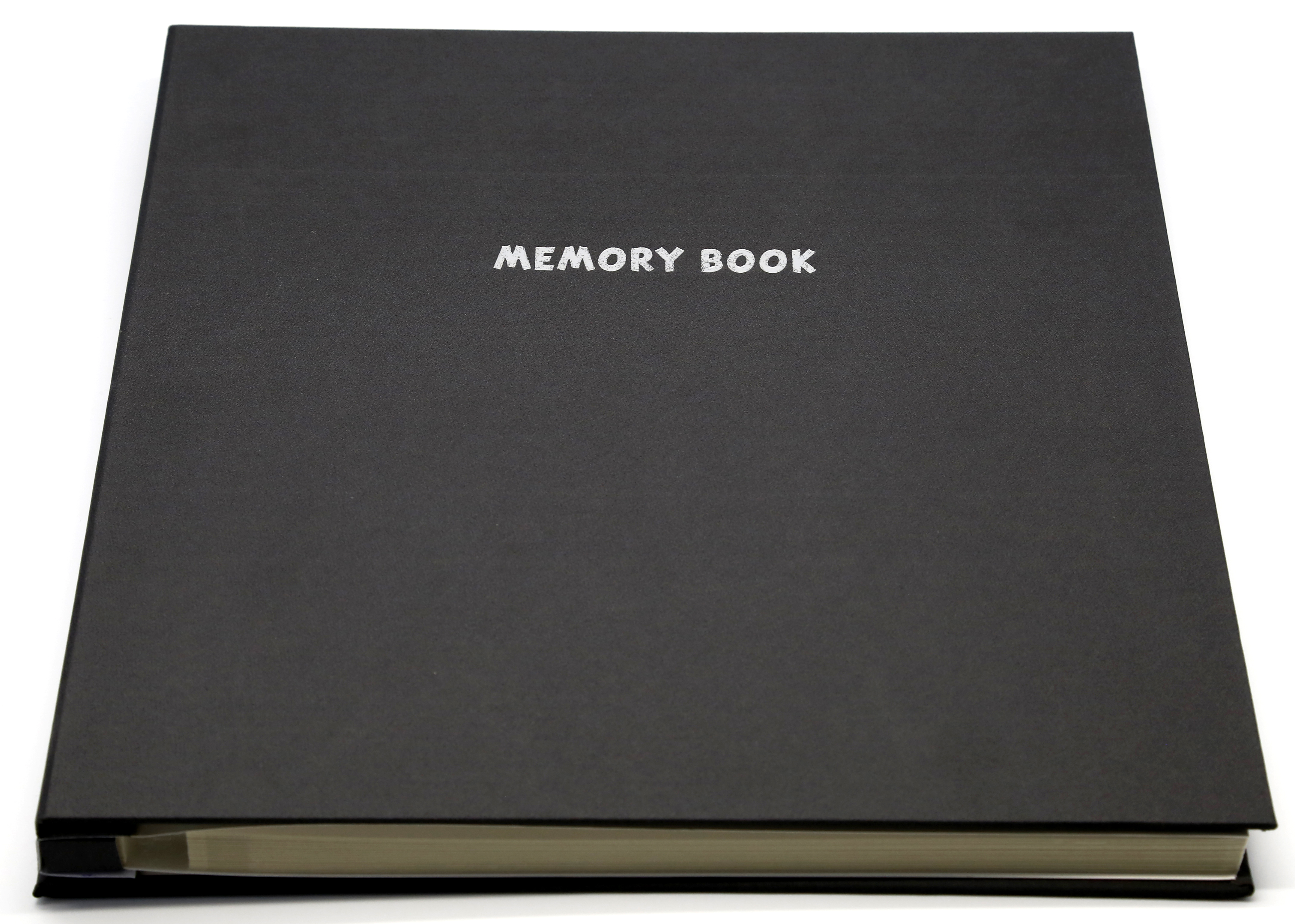 Egy zárt fekete könyv "MEMORY BOOK" felirattal, ezüst betűkkel, fehér felületen.