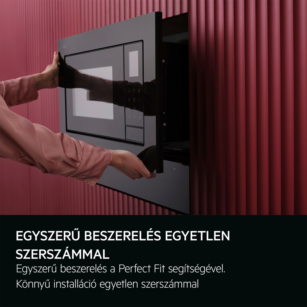 Kezek fekete mikrohullámú sütőt szerelnek fel egy piros, textúrázott falra, szöveggel.