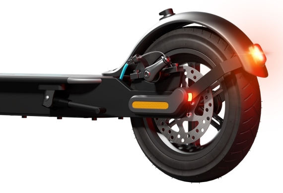 Tył czarnej hulajnogi ze światłem tylnym. Widoczna opona. Białe tło.