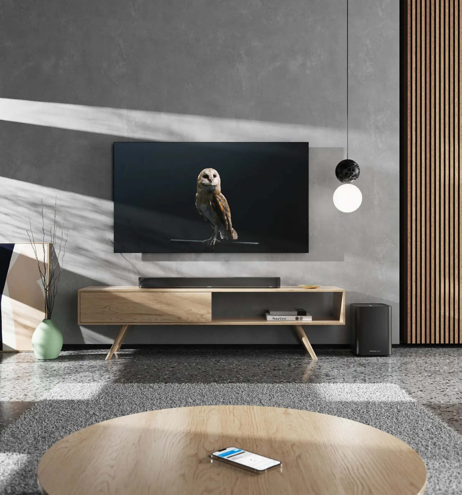 Un salon avec une TV, une image de hibou, une barre de son et une table ronde avec un téléphone.