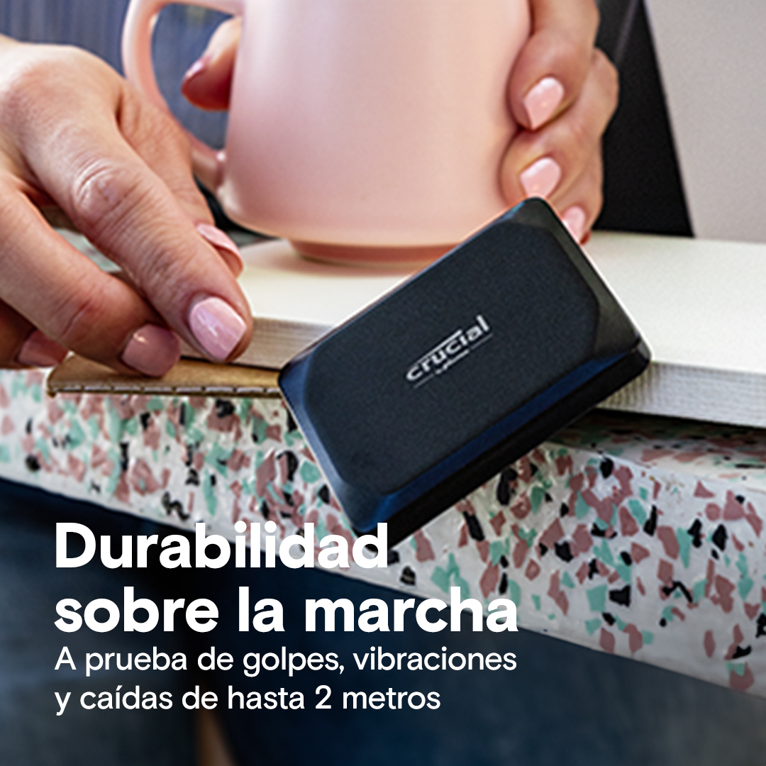 Manos sosteniendo un SSD externo Crucial negro, con texto en una superficie colorida.