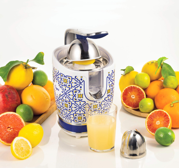Exprimidor con frutas alrededor, un vaso de zumo.
