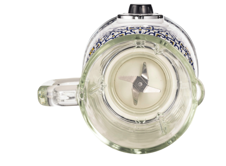 Vista superior de una licuadora de vidrio transparente con base decorativa y cuchilla, fondo blanco.