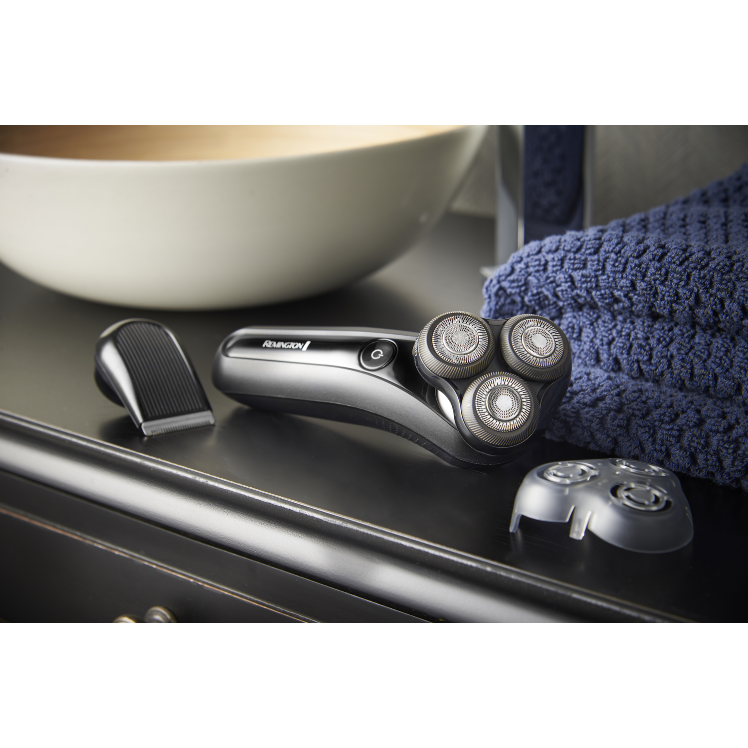 A silver and black electric shaver with three heads, a trimmer, and a bowl.