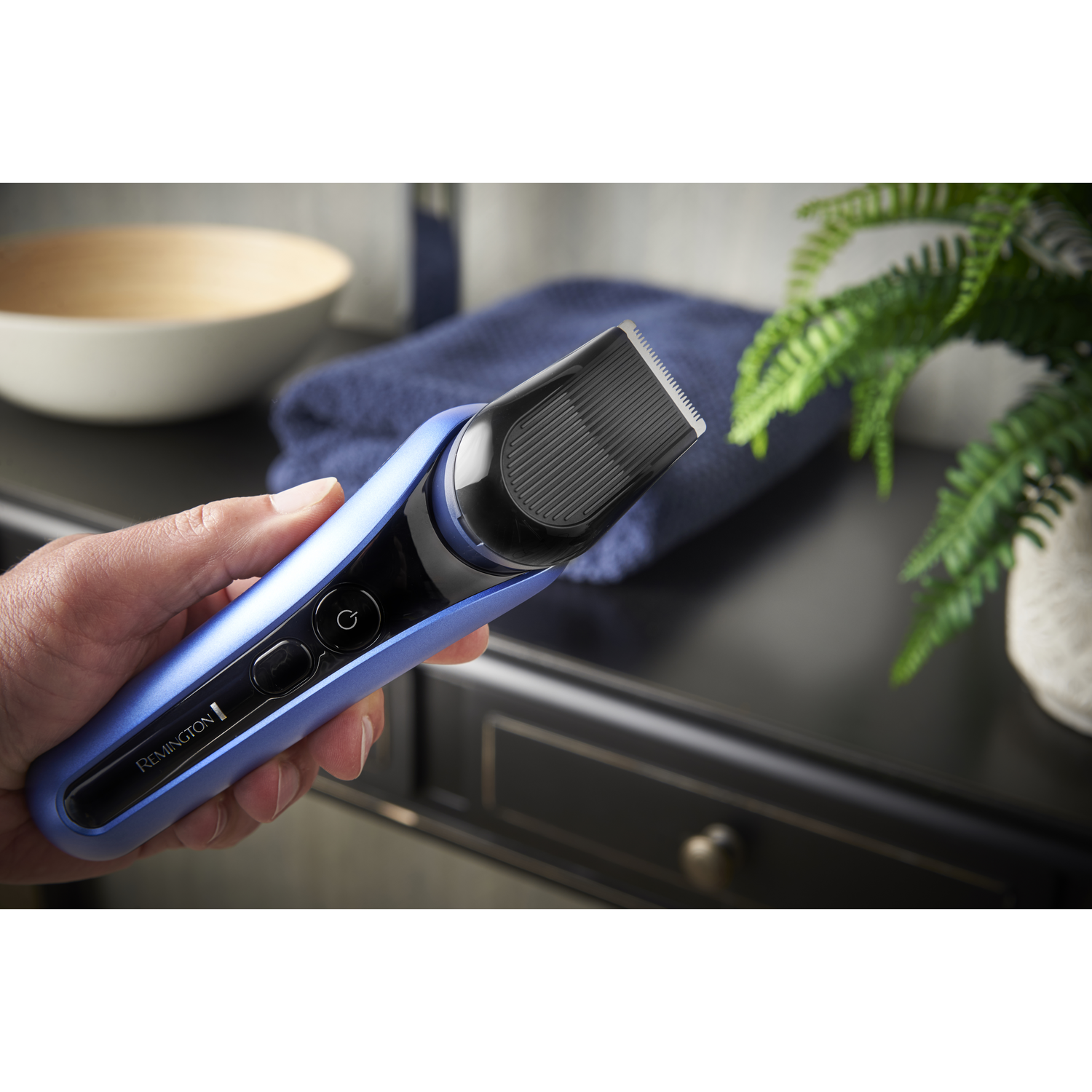 A person's hand holding a blue Remington beard trimmer.