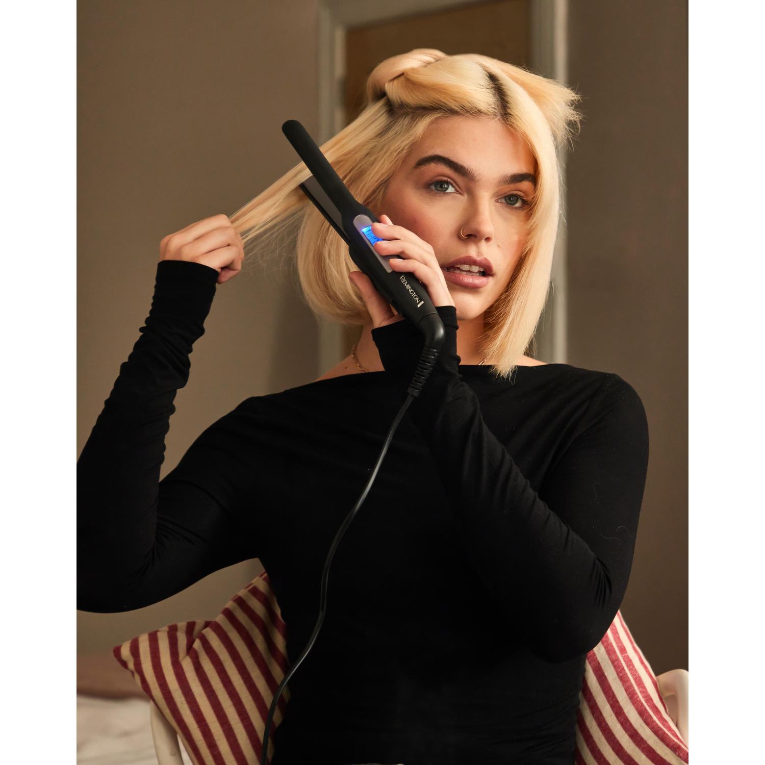 Woman with blonde hair, using a black hair straightener.