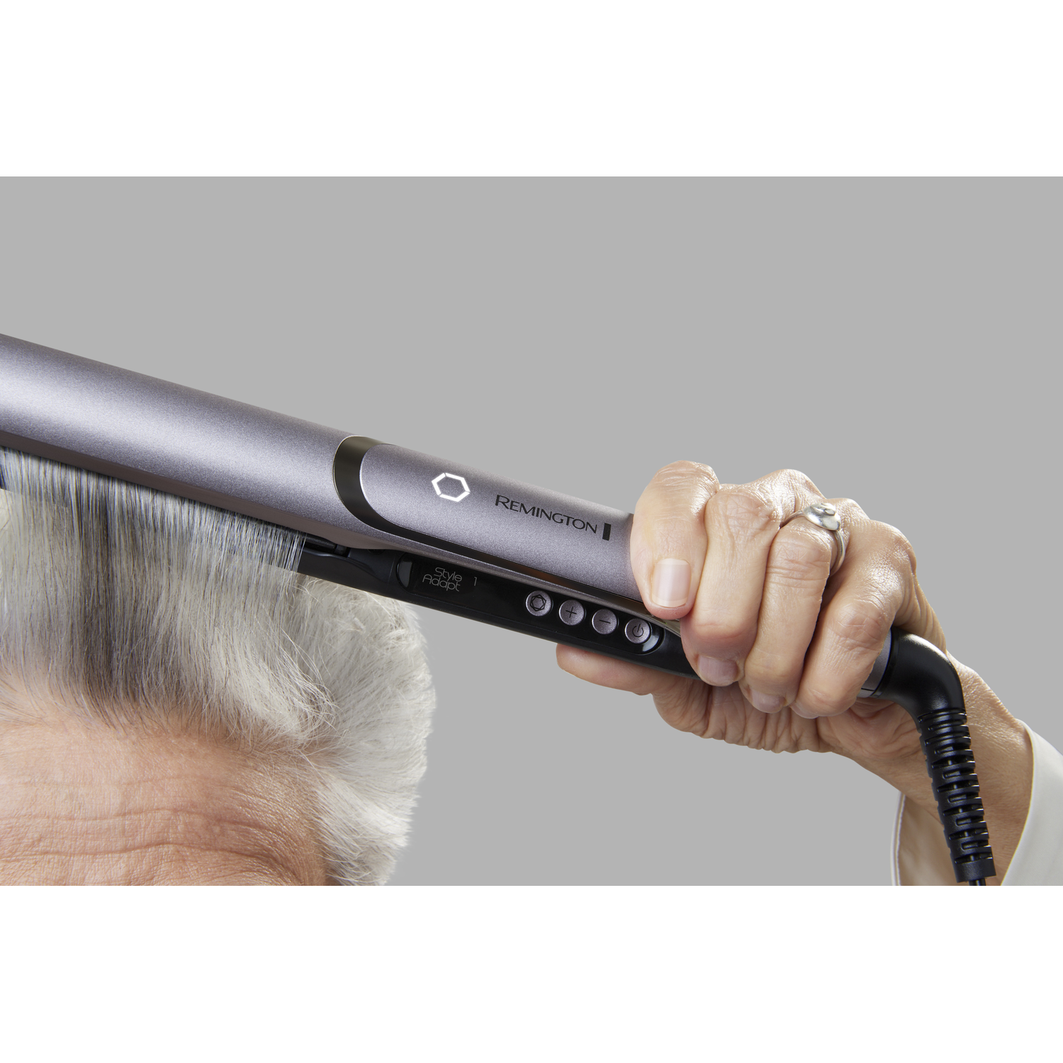 A person using a silver Remington hair straightener on grey hair, close-up shot.
