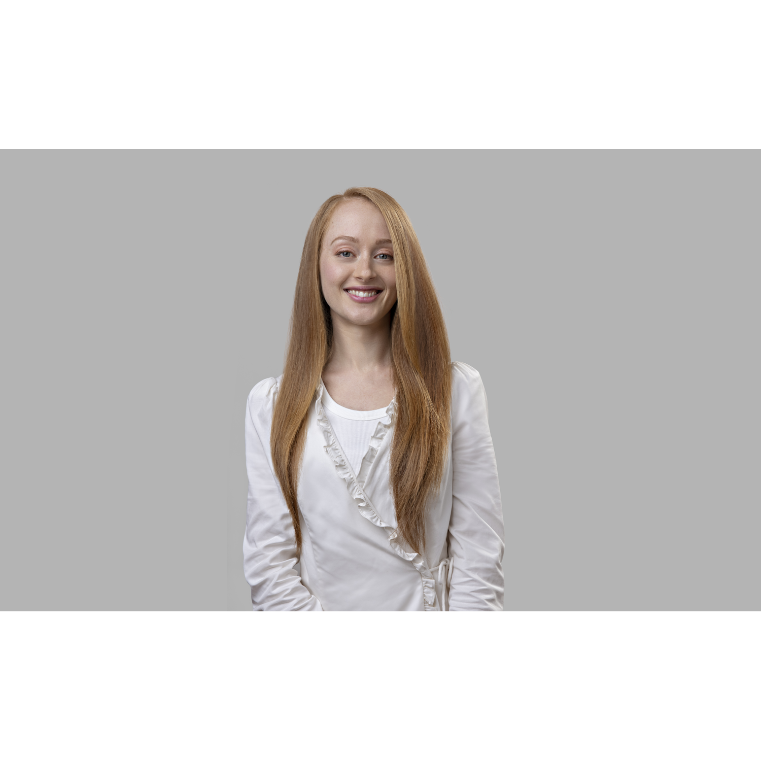 A young woman with long red hair smiles at the camera, wearing a white blouse.