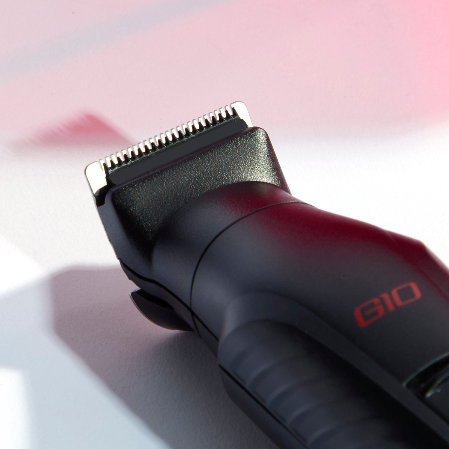 A black hair trimmer with red G10 text and a silver blade, on a white and pink background.