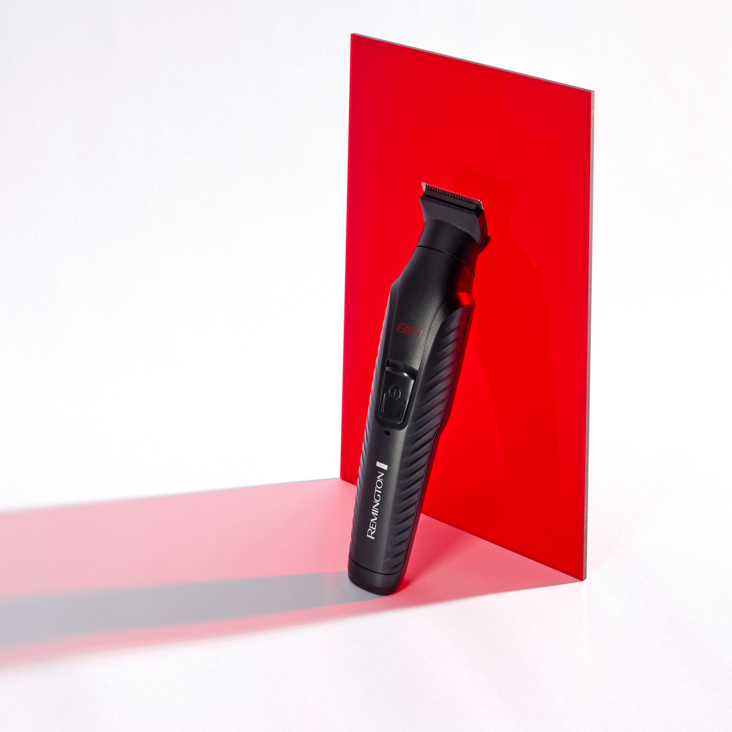 Black Remington beard trimmer against a red background, with its shadow.