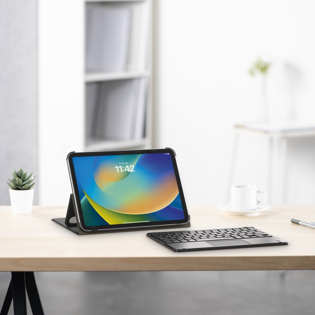 Tablet mit Tastatur auf einem Schreibtisch. Der Bildschirm zeigt die Uhrzeit an. Eine kleine Pflanze und eine Tasse sind auch auf dem Schreibtisch.