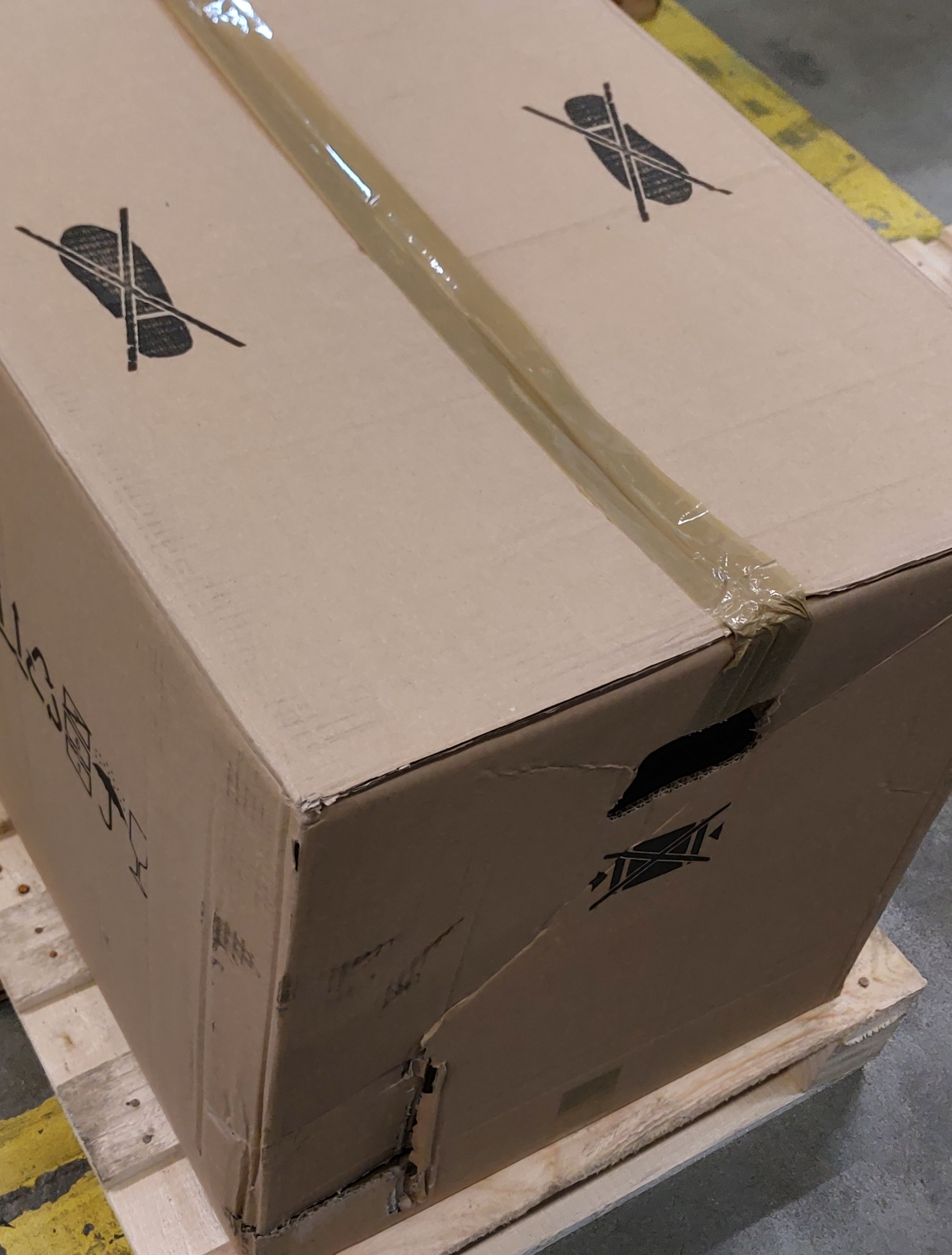 Duże kartonowe pudełko na drewnianej palecie, z taśmą klejącą i etykietami wysyłkowymi.