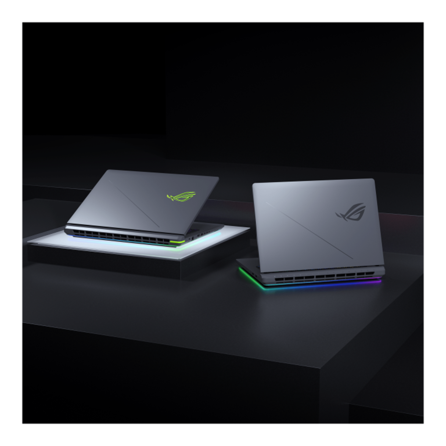 Two gray laptops, angled view, lit up. Green and blue lights on the bottom.