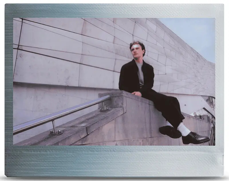 Mężczyzna siedzi na betonowym gzymsie obok budynku o minimalistycznym designie.