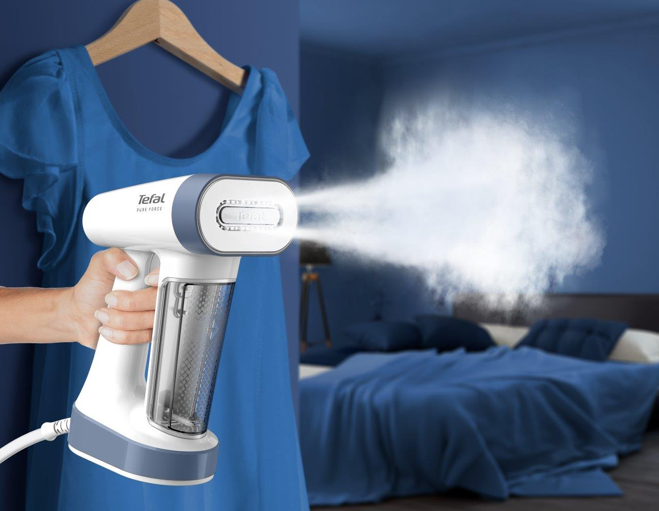 Biała i niebieska parownica do odzieży emitująca parę. Sukienka wisi w tle.