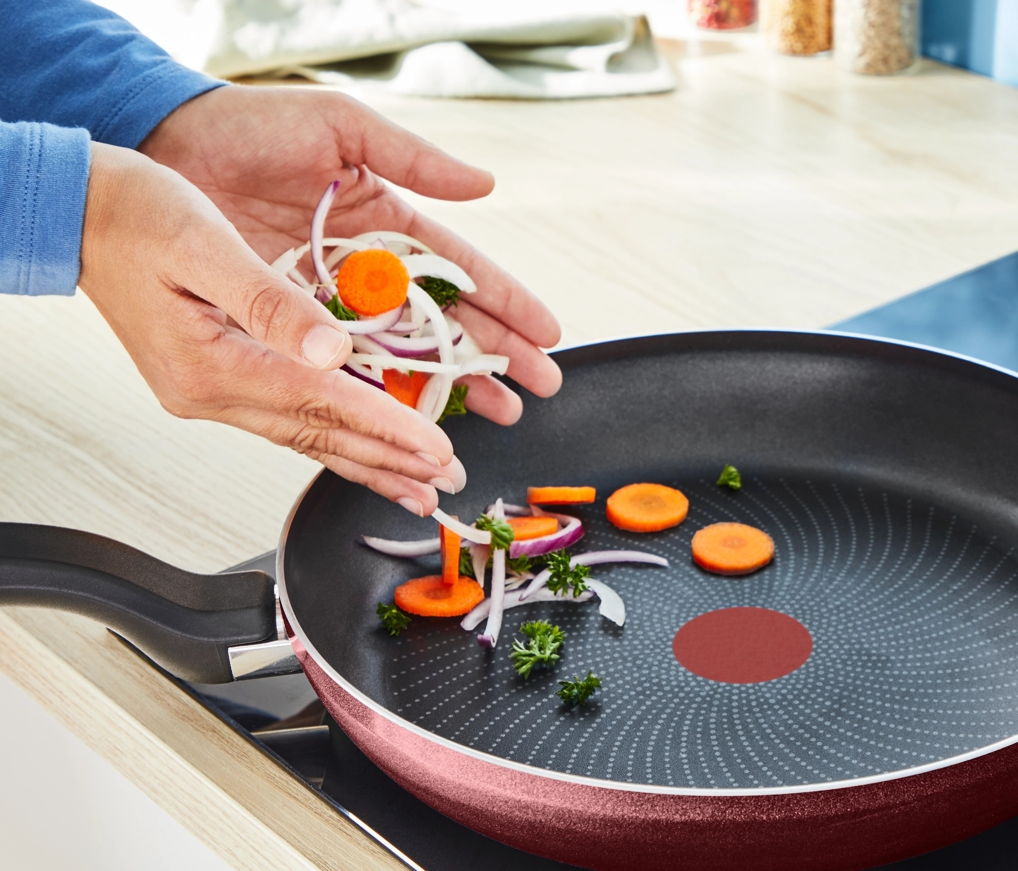 Dłonie dodają pokrojone warzywa do patelni na kuchence.