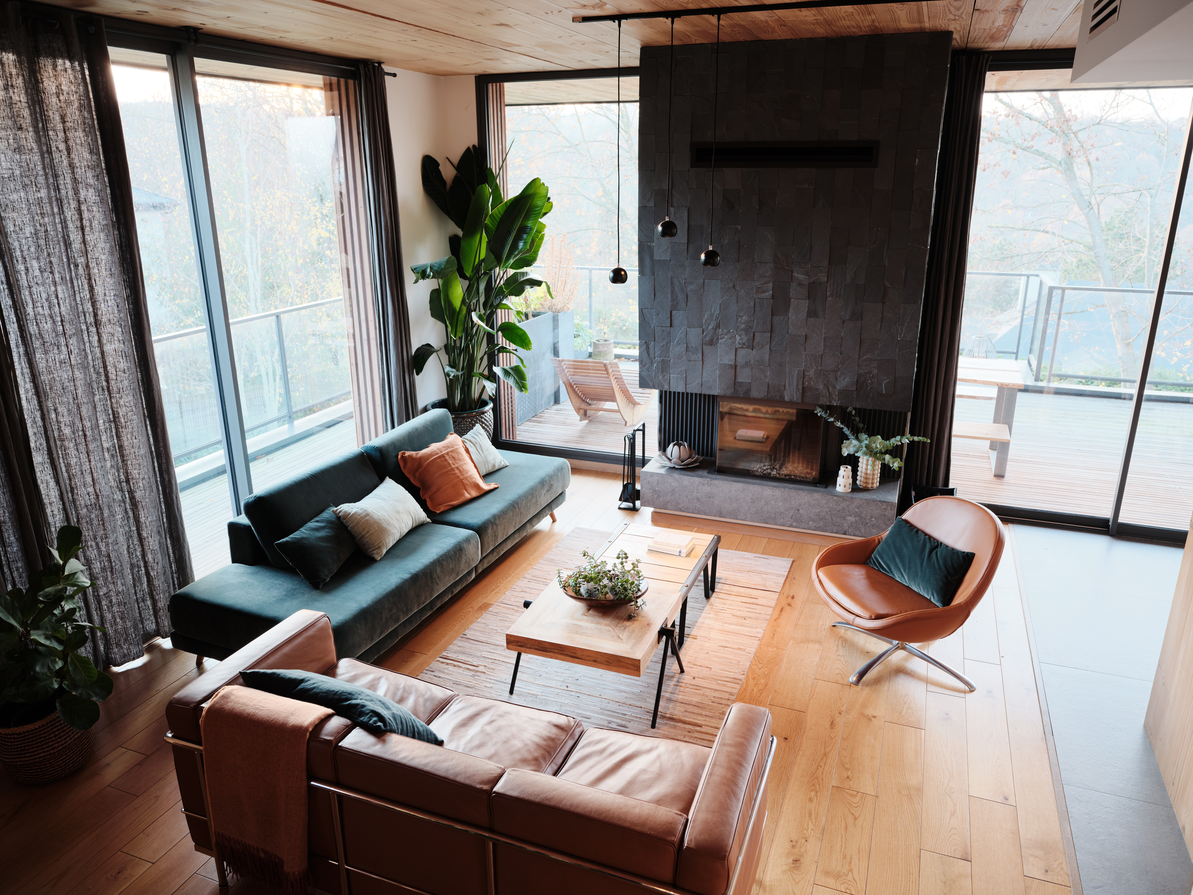 Ein modernes Wohnzimmer mit einem grünen Sofa, einem braunen Sofa und großen Fenstern.