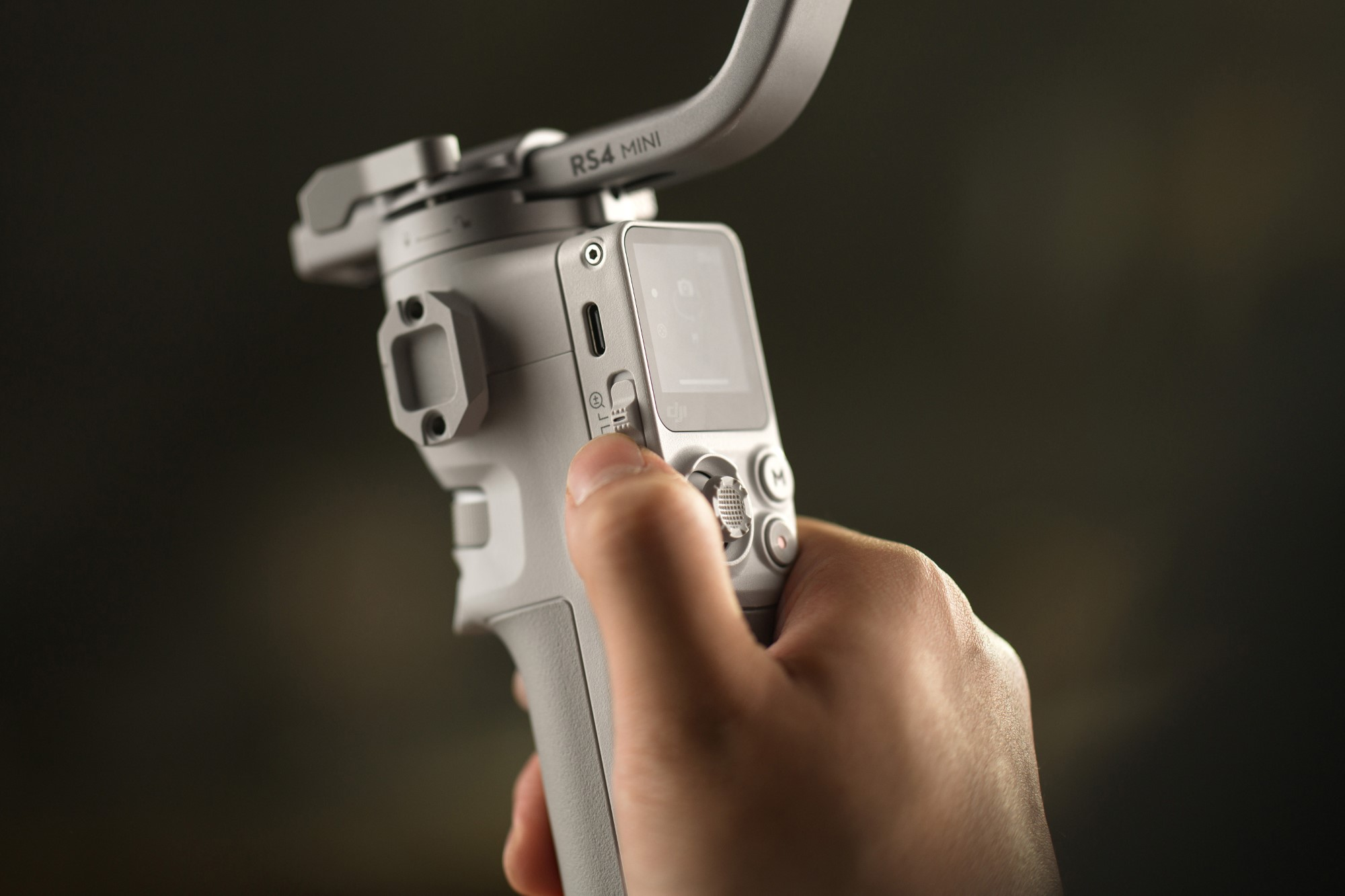 Ręka trzymająca szary gimbal z małym ekranem, przyciskami i nazwą RS4 MINI.