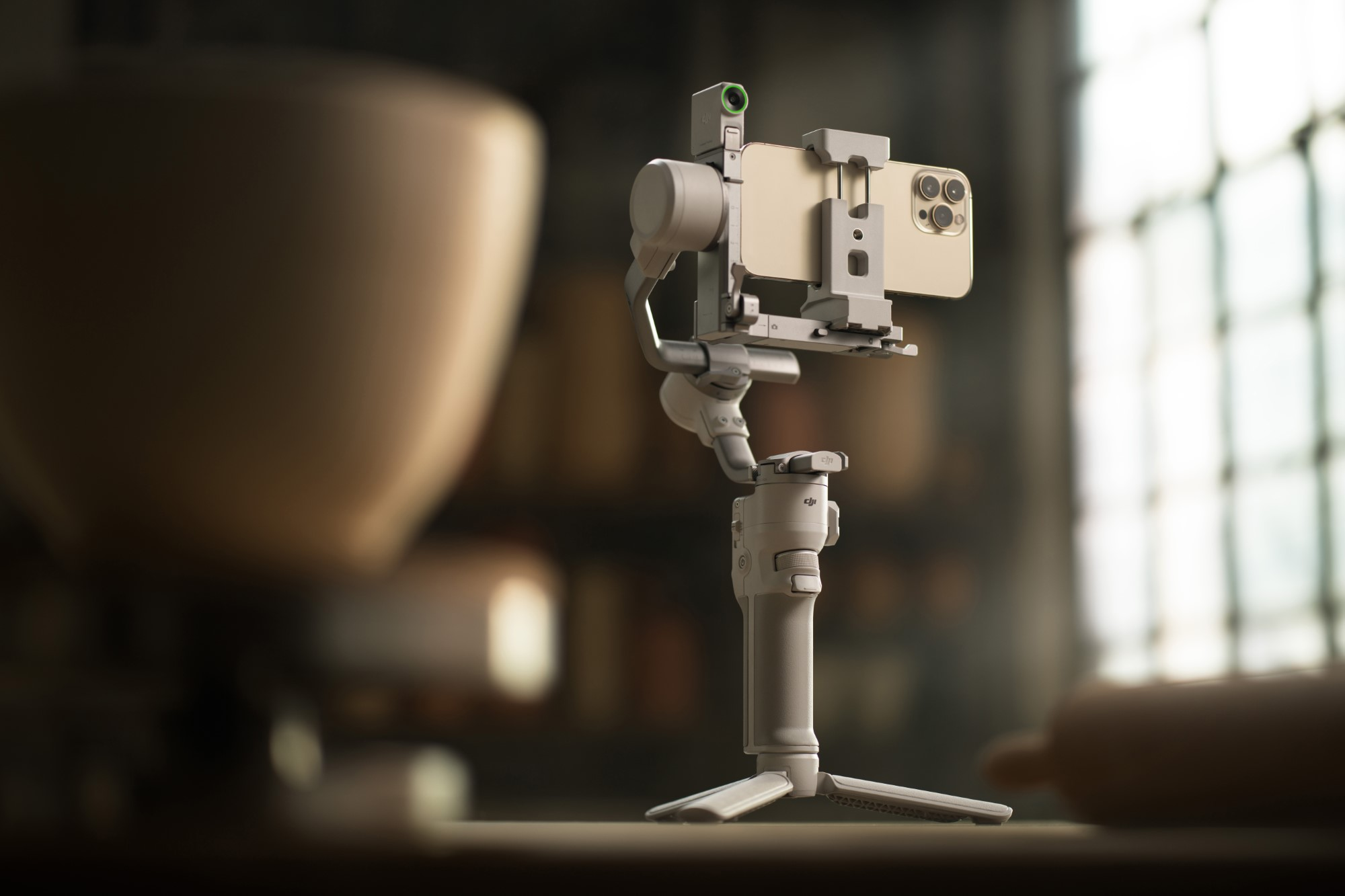Smartfon na statywie z gimbalem, nagrywanie. Jasny drewniany stół, rozmyte tło.
