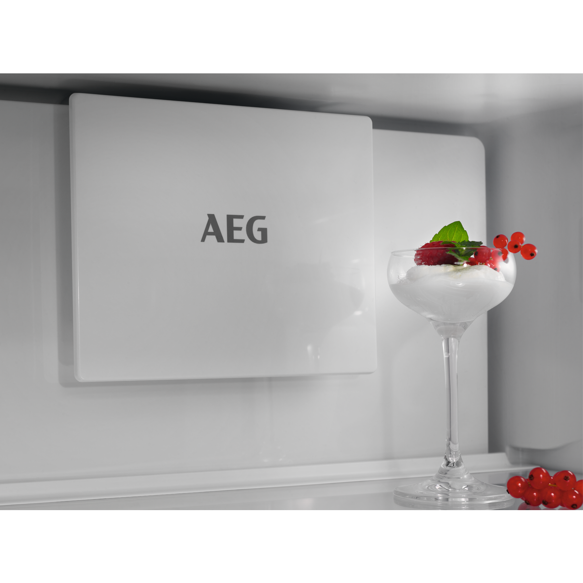Egy hűtőszekrény belsejében desszert egy pohárban piros bogyókkal és egy fehér AEG panellel.