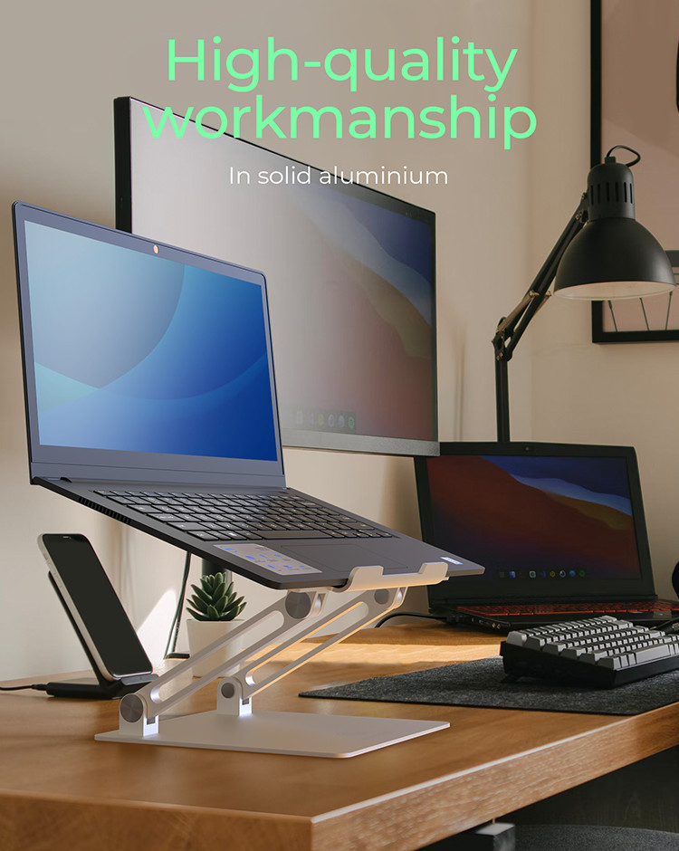 Ein Laptop auf einem silbernen Ständer. Ein Monitor, eine Schreibtischlampe und andere Laptops im Hintergrund.
