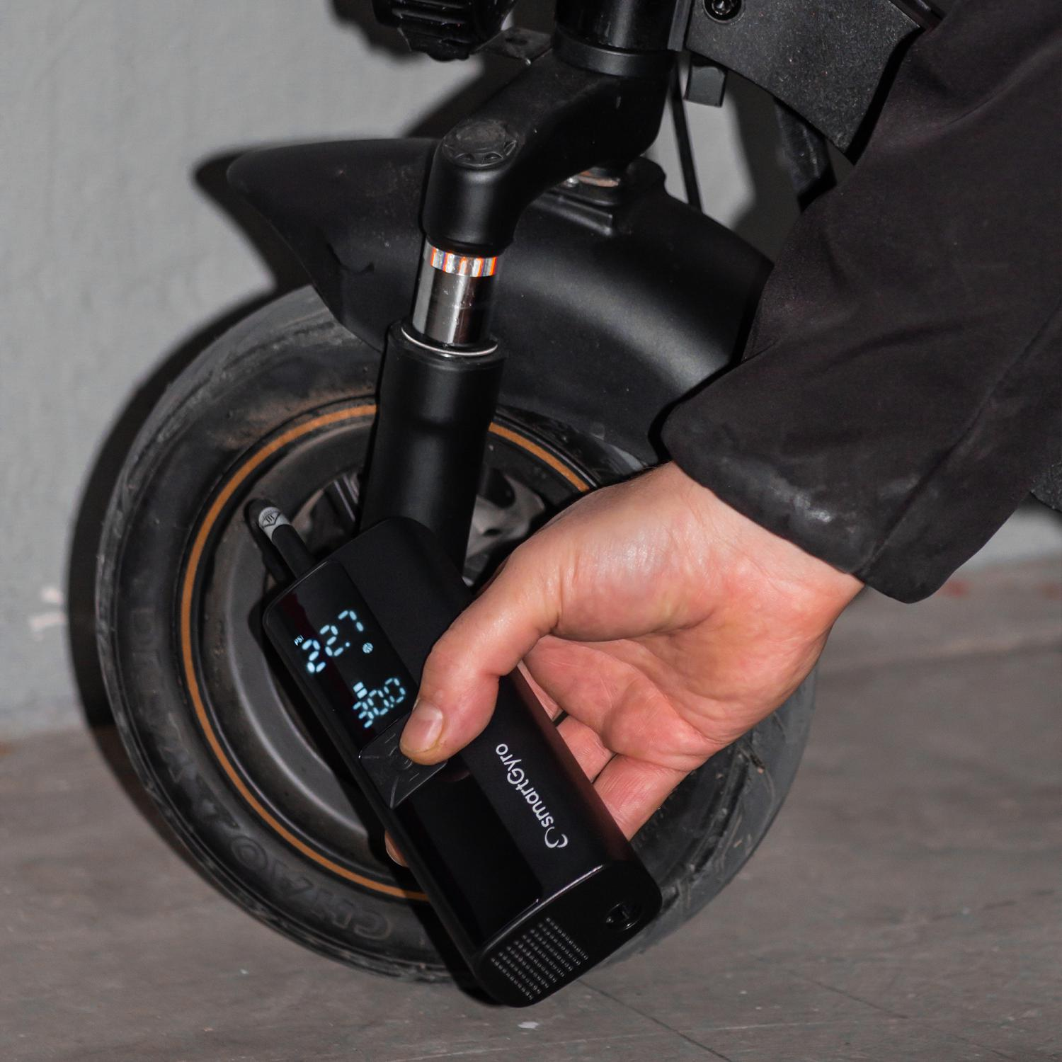 Una persona infla un neumático de scooter con una bomba de aire digital negra. El neumático está adjunto.