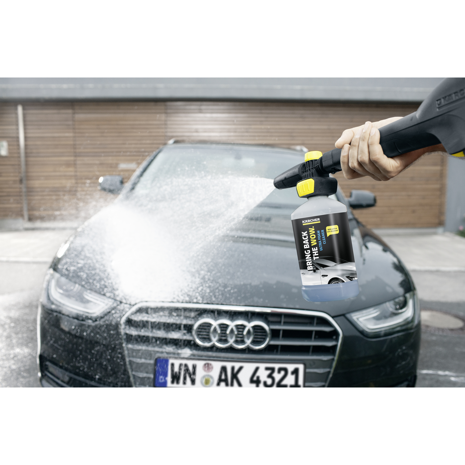 A person spraying a car with foam from a Kärcher bottle. The car is in a driveway.
