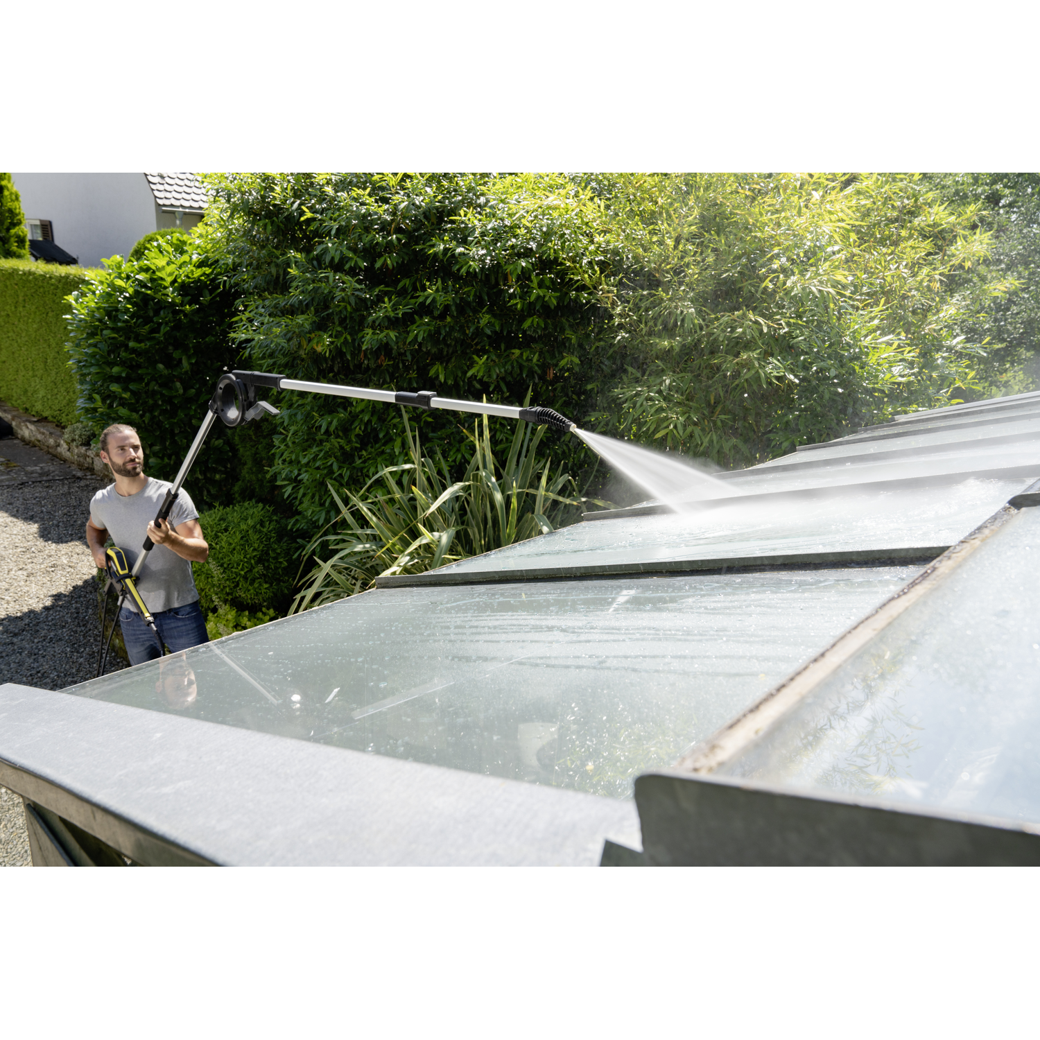 A man is cleaning a greenhouse roof with a pressure washer.