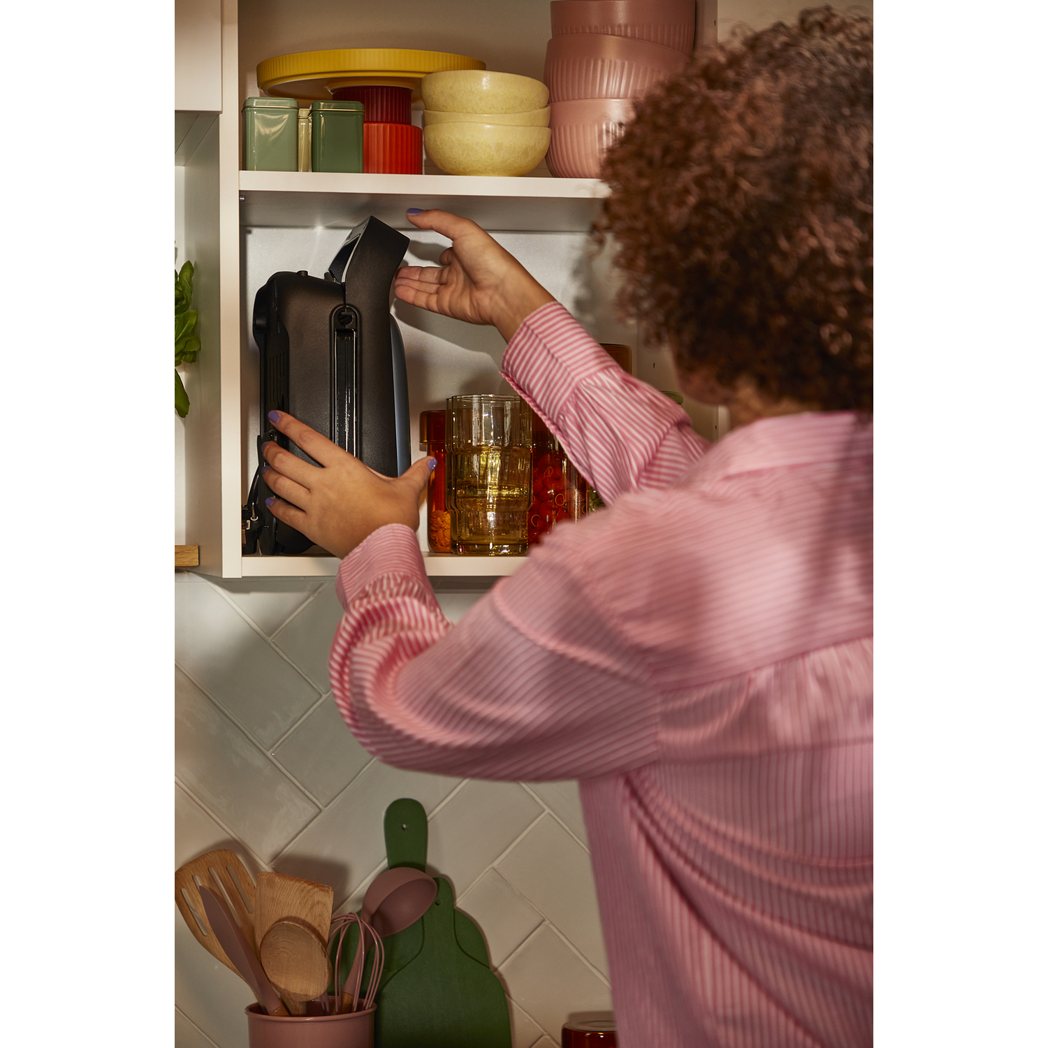 A person reaching into a white cabinet to put away a black bag.