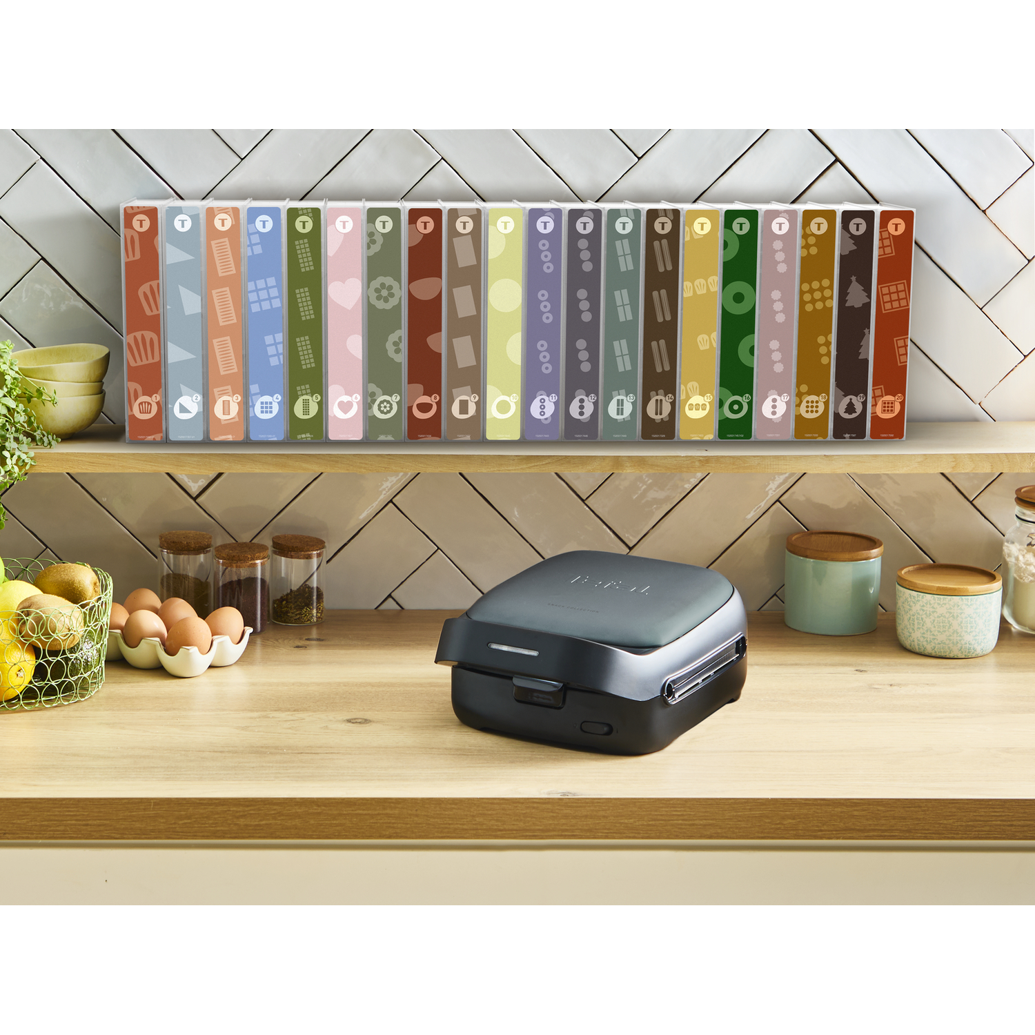 A Tefal snack maker with various snack plates displayed behind it on a counter.