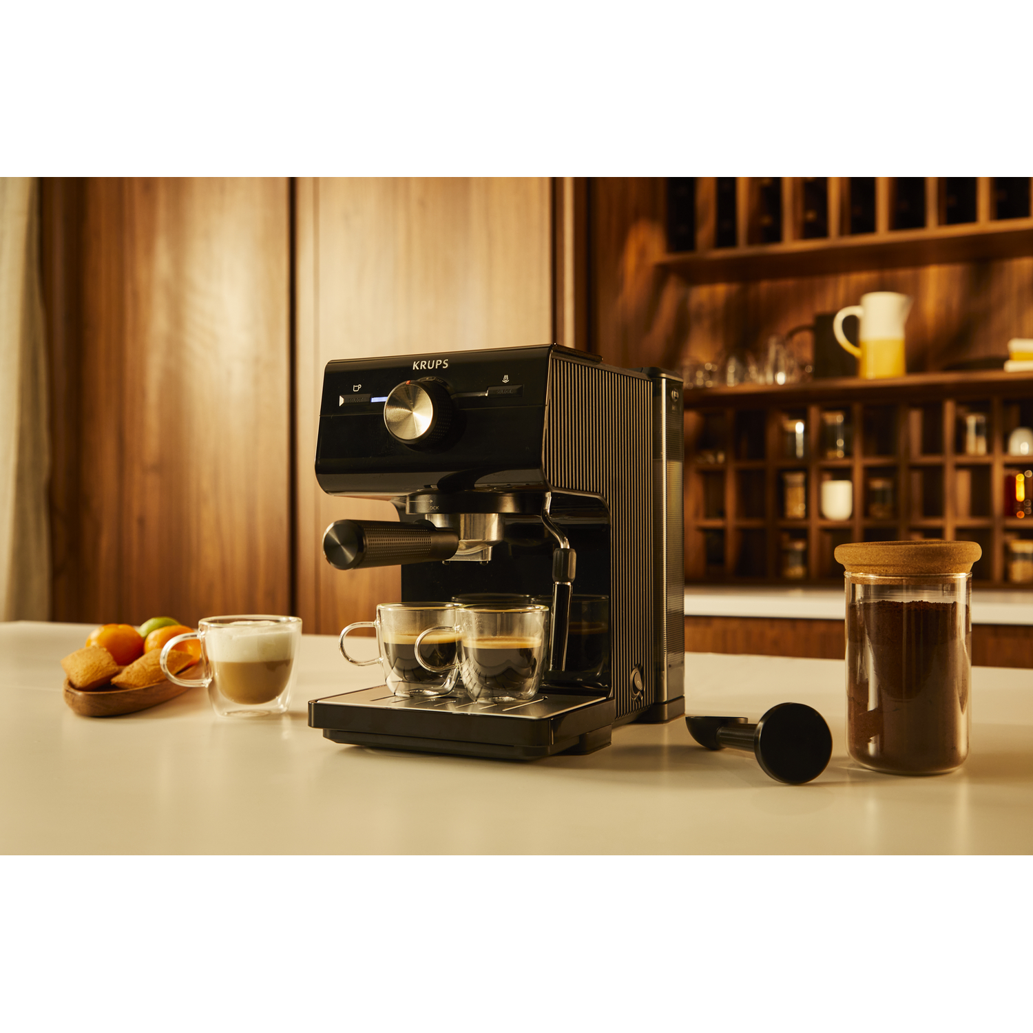 Zwarte Krups espressomachine met twee kopjes, een koffiemolen en koekjes.
