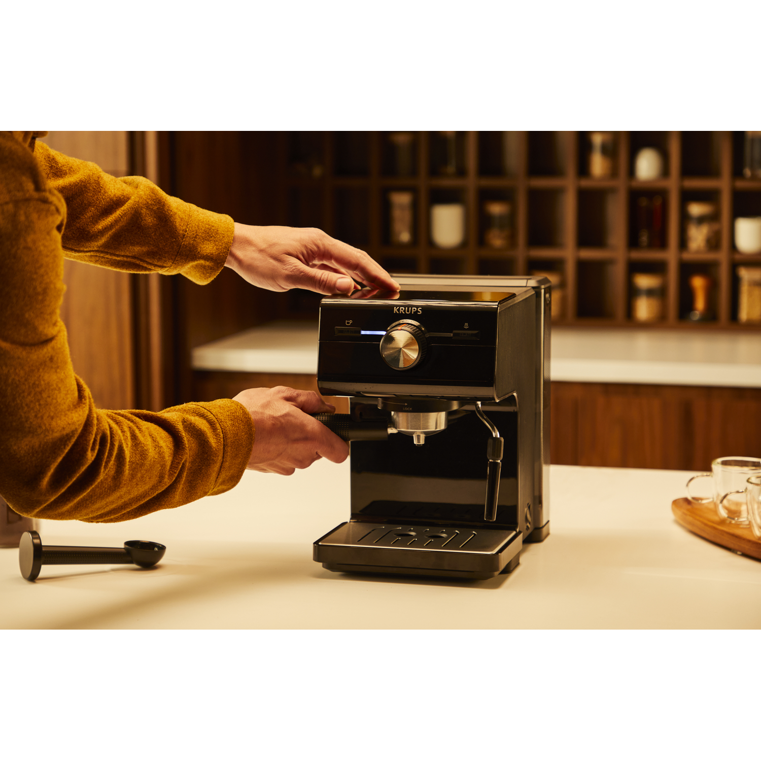 Een persoon gebruikt een Krups espressomachine op een wit aanrecht in een keuken.