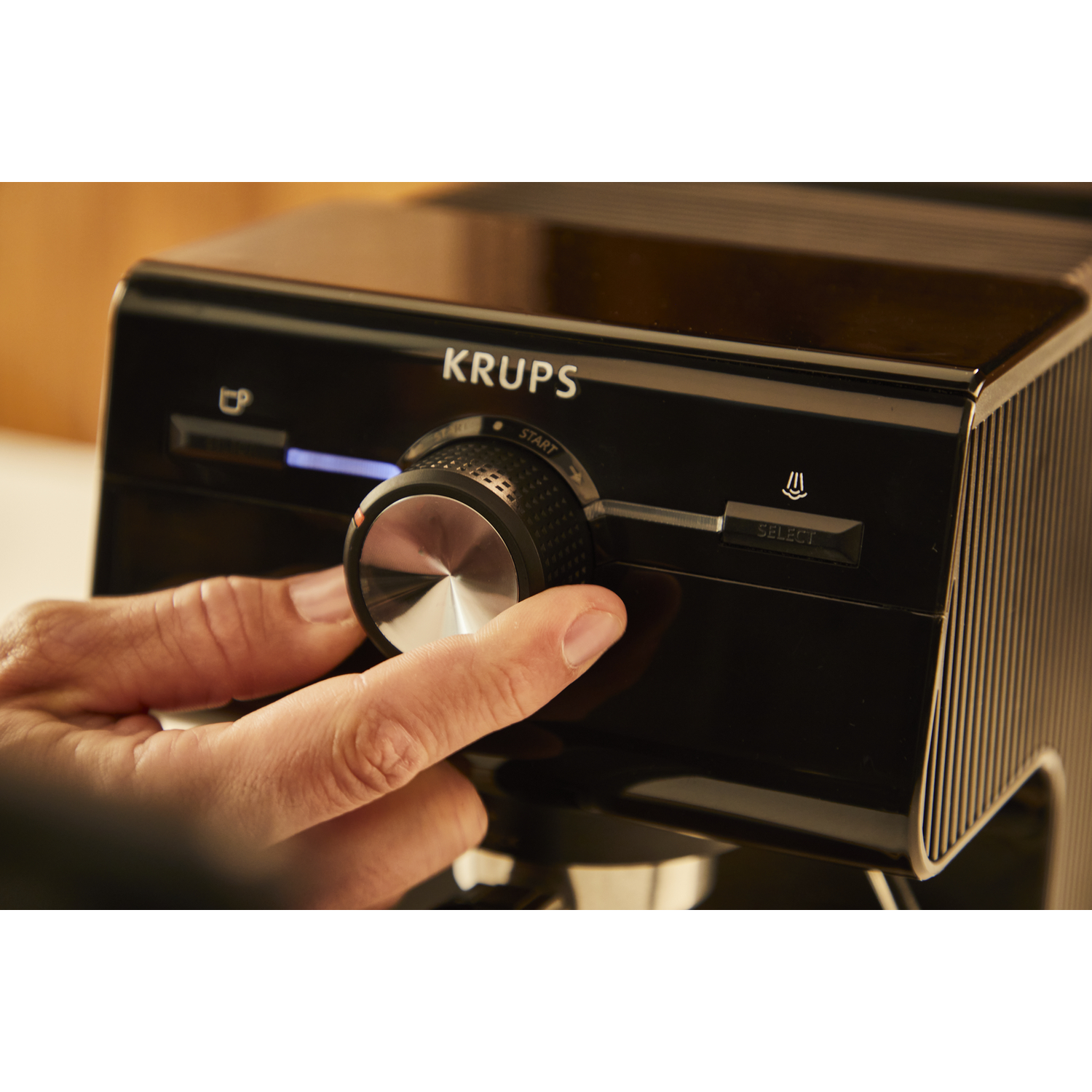 Close-up van een zwarte Krups koffiemachine met een hand die aan een draaiknop draait. Knoppen zichtbaar.
