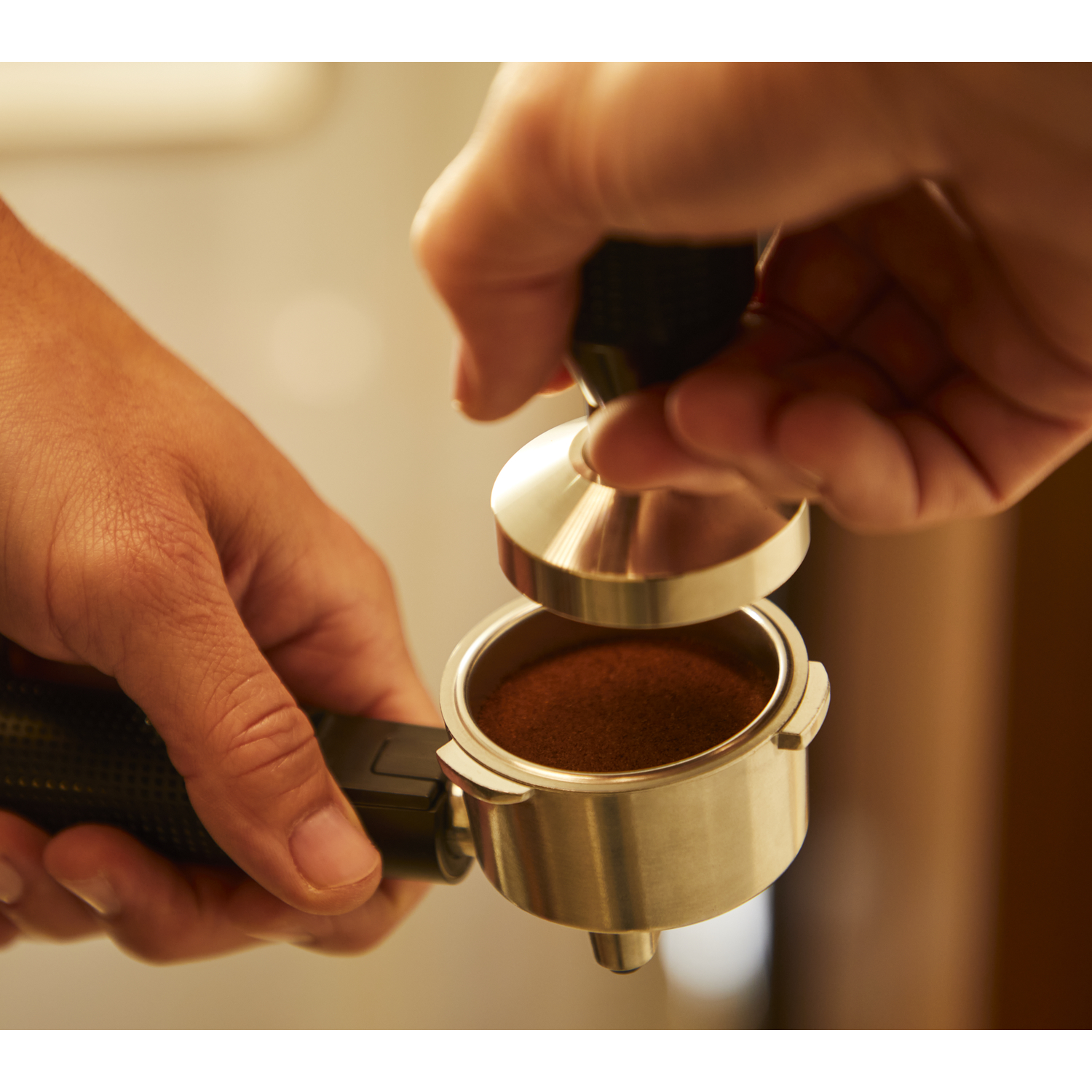 Handen gebruiken een tamper om gemalen koffie in een portafilter te persen.